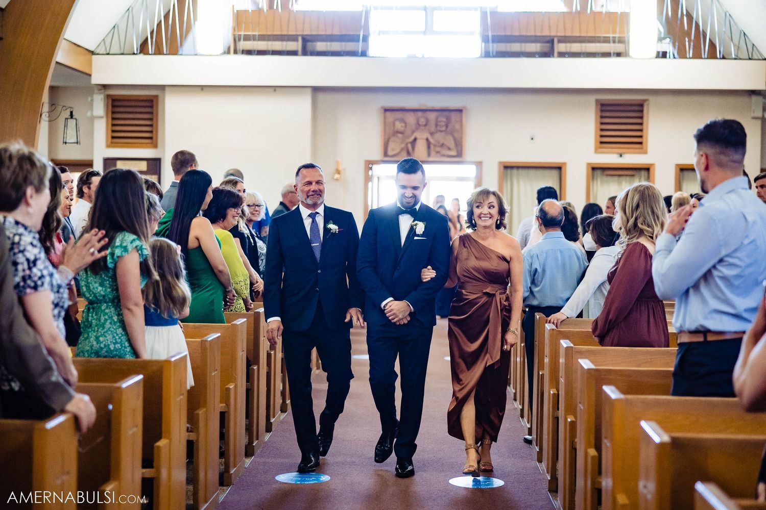 Groom smiling in black tuxedo with white boutonniere during wedding ceremony.