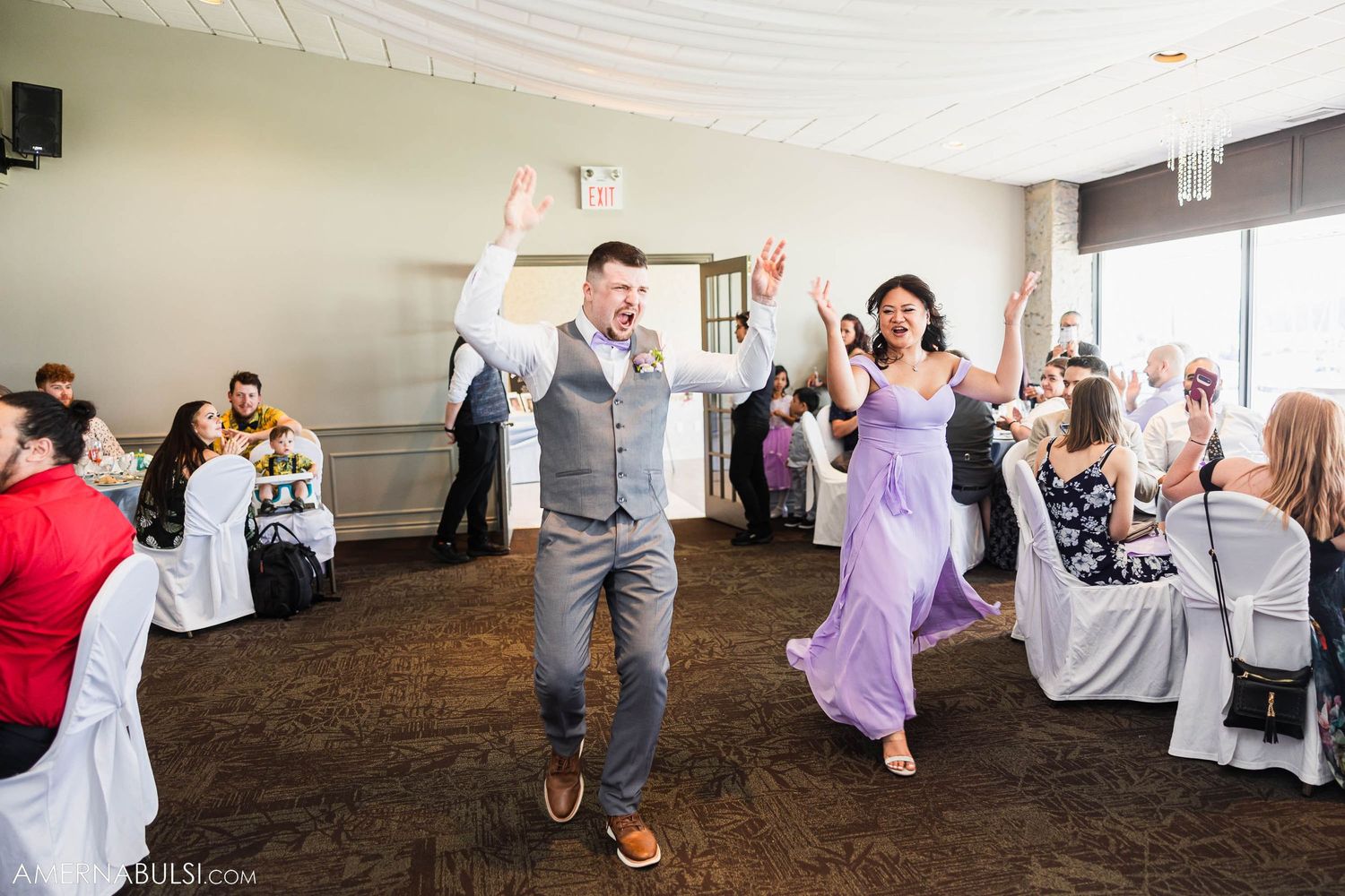 Reception celebration with energetic dancing in venue featuring dark carpeting and white chairs.