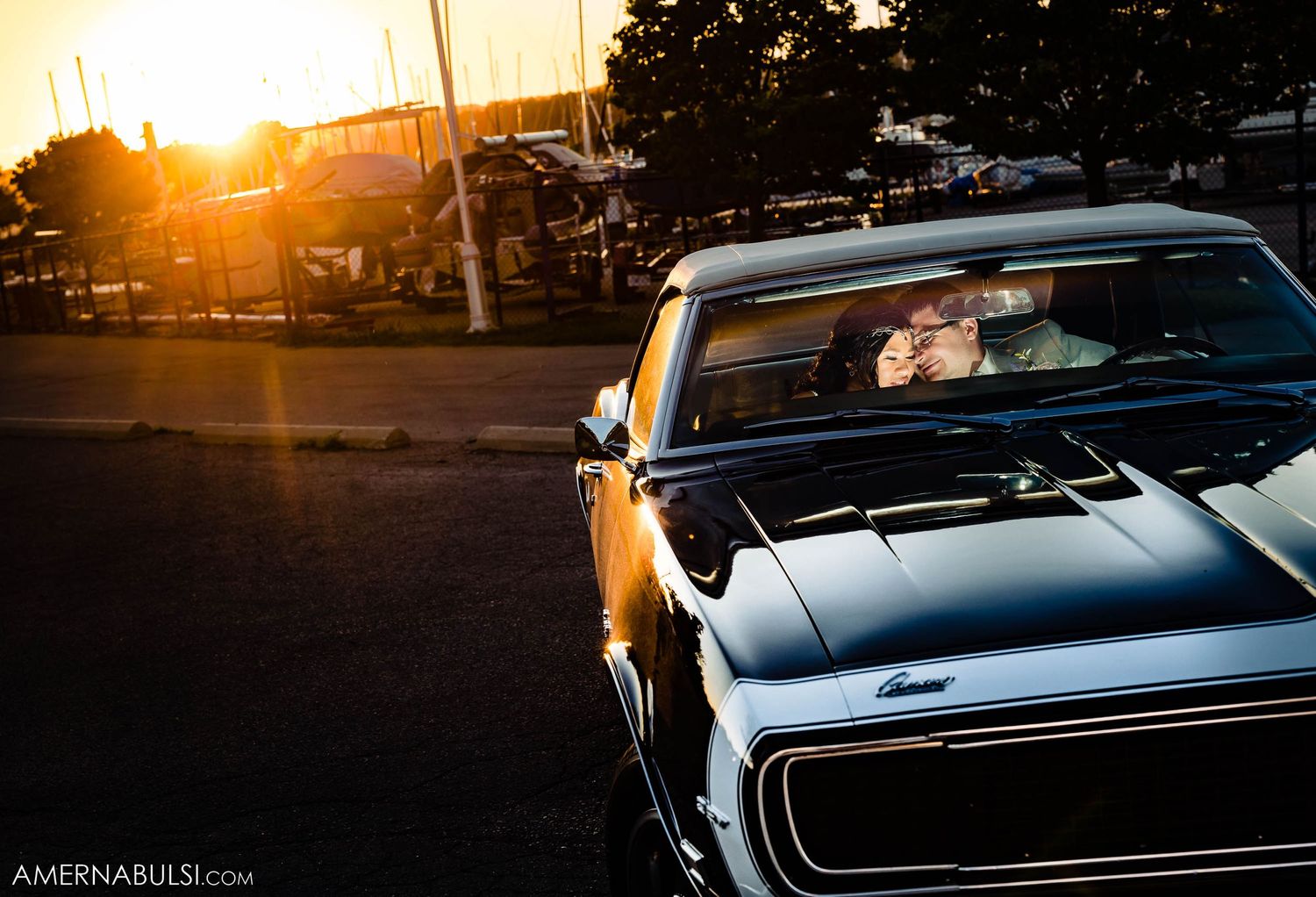 Classic car silhouetted against a golden sunset in an urban setting.