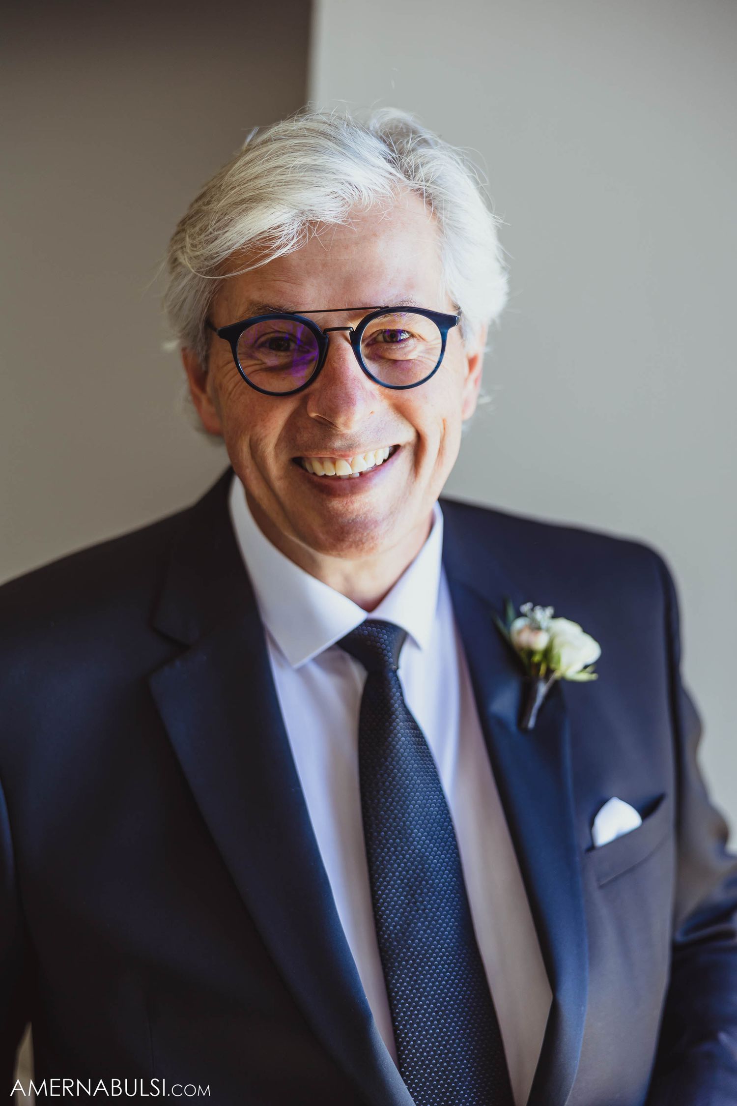 Groom in navy suit and glasses smiles warmly while wearing a boutonniere.