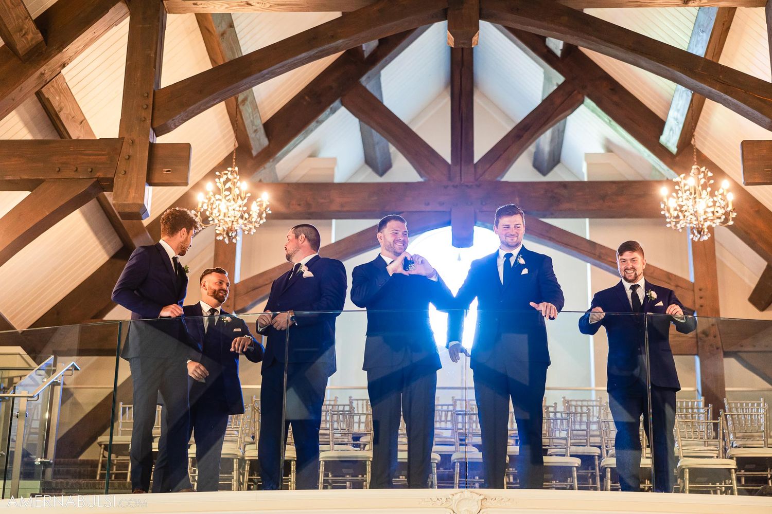 Wedding party performs choreographed dance under vaulted wooden ceiling with chandeliers.