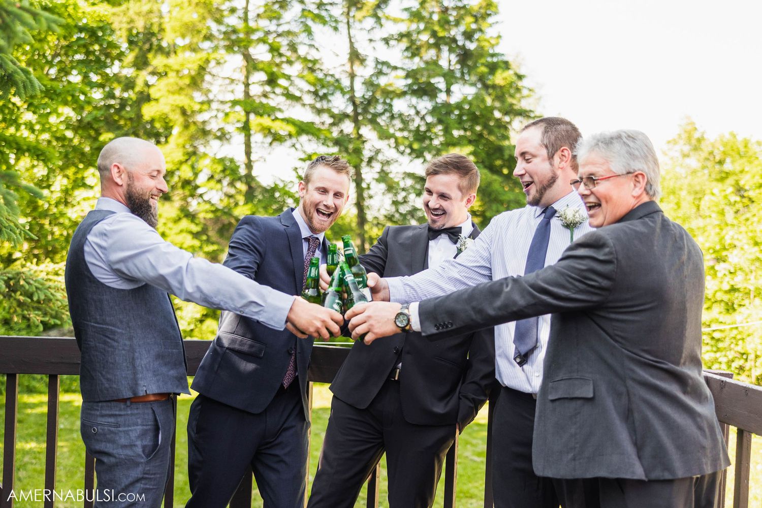 Groomsmen share a celebratory toast outdoors on a sunny wedding day.