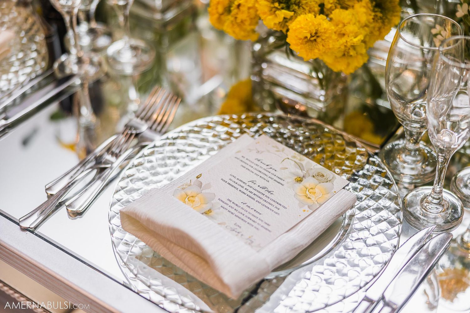 Formal place setting with silver charger plate, menu card, and yellow floral accents.