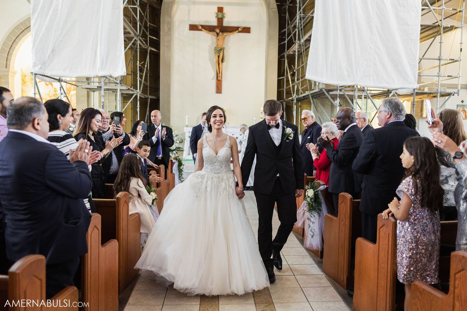 Wedding guests applaud as the newlyweds make their way down the church aisle.