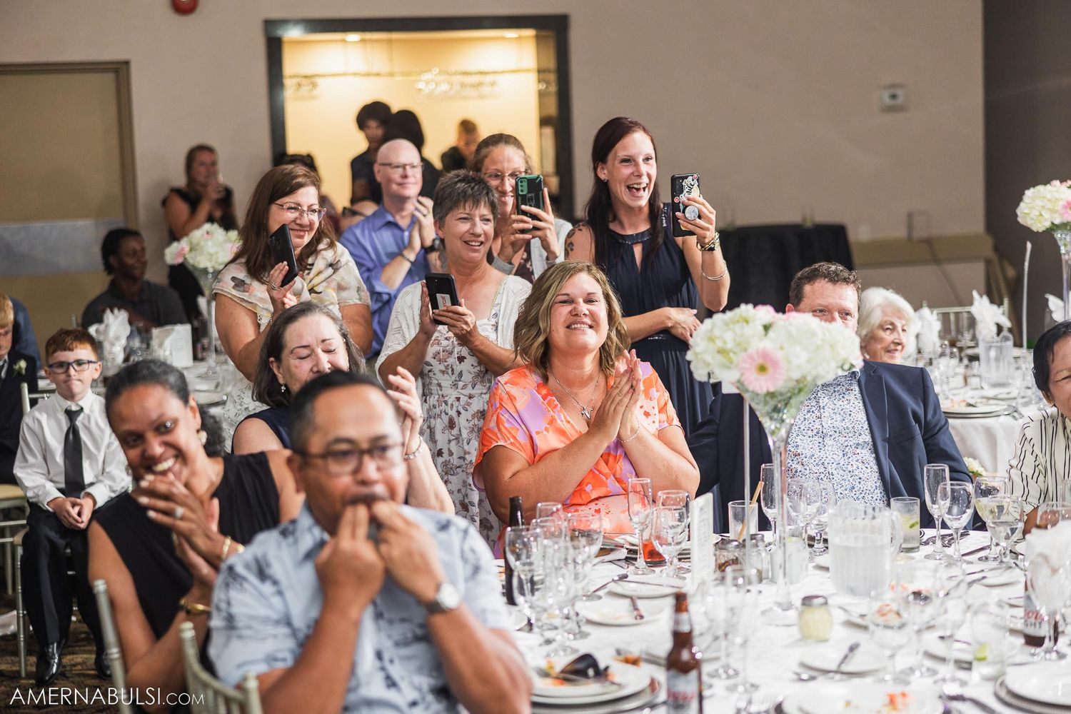 Wedding reception guests react emotionally during speeches at elegant table setting.