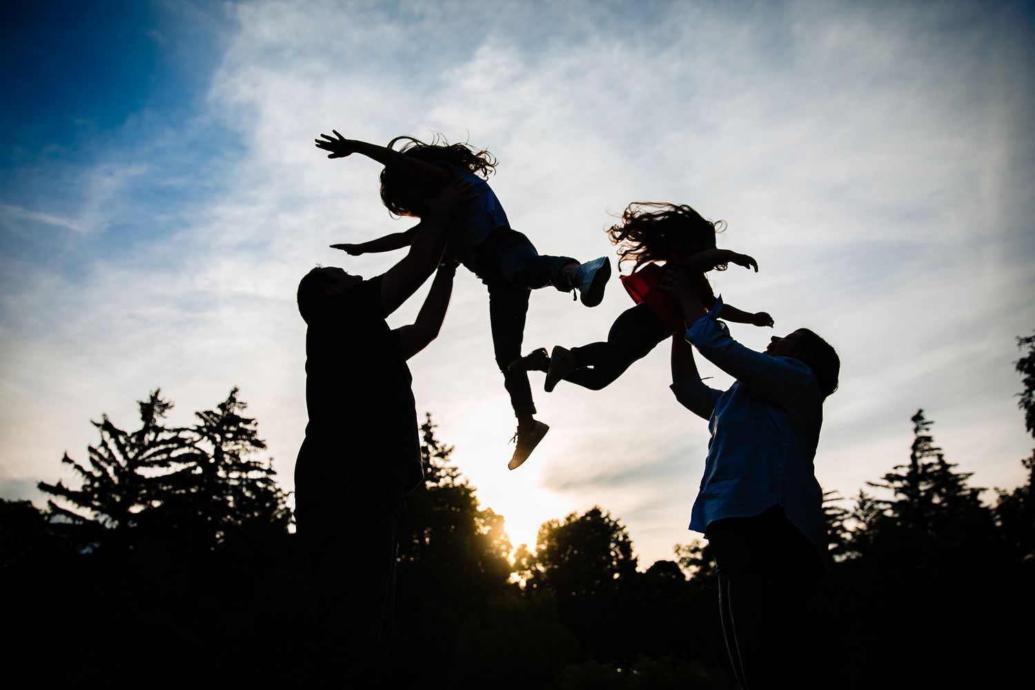 Silhouetted figures dance and leap against a dramatic cloudy sky at sunset.