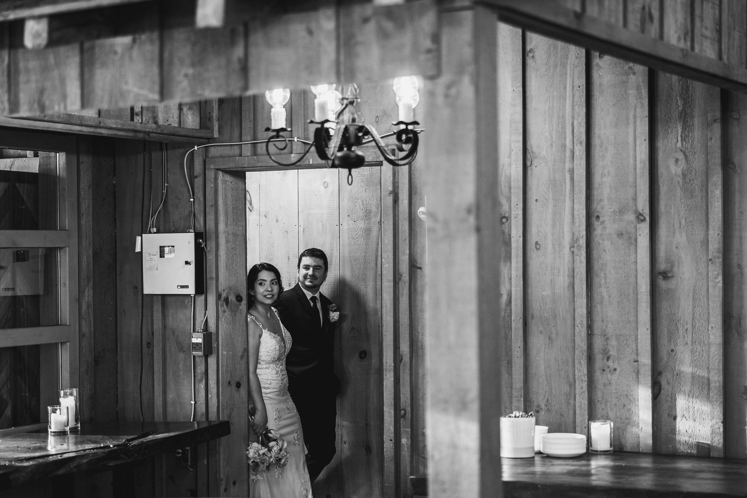 Black and white photo of bride and groom standing in rustic barn wedding venue doorway.