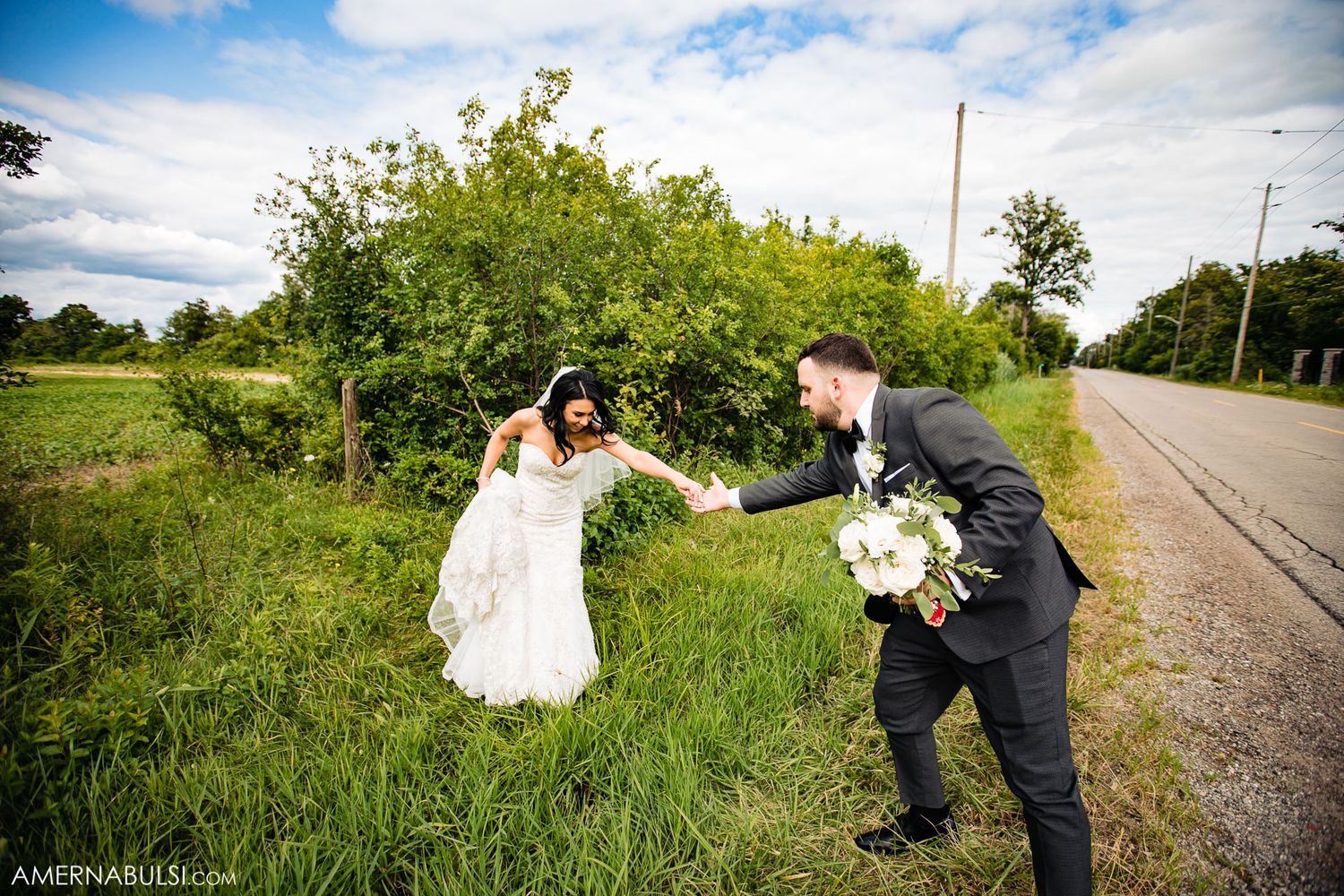 Newlyweds playfully walking together on rural road with green foliage in background.