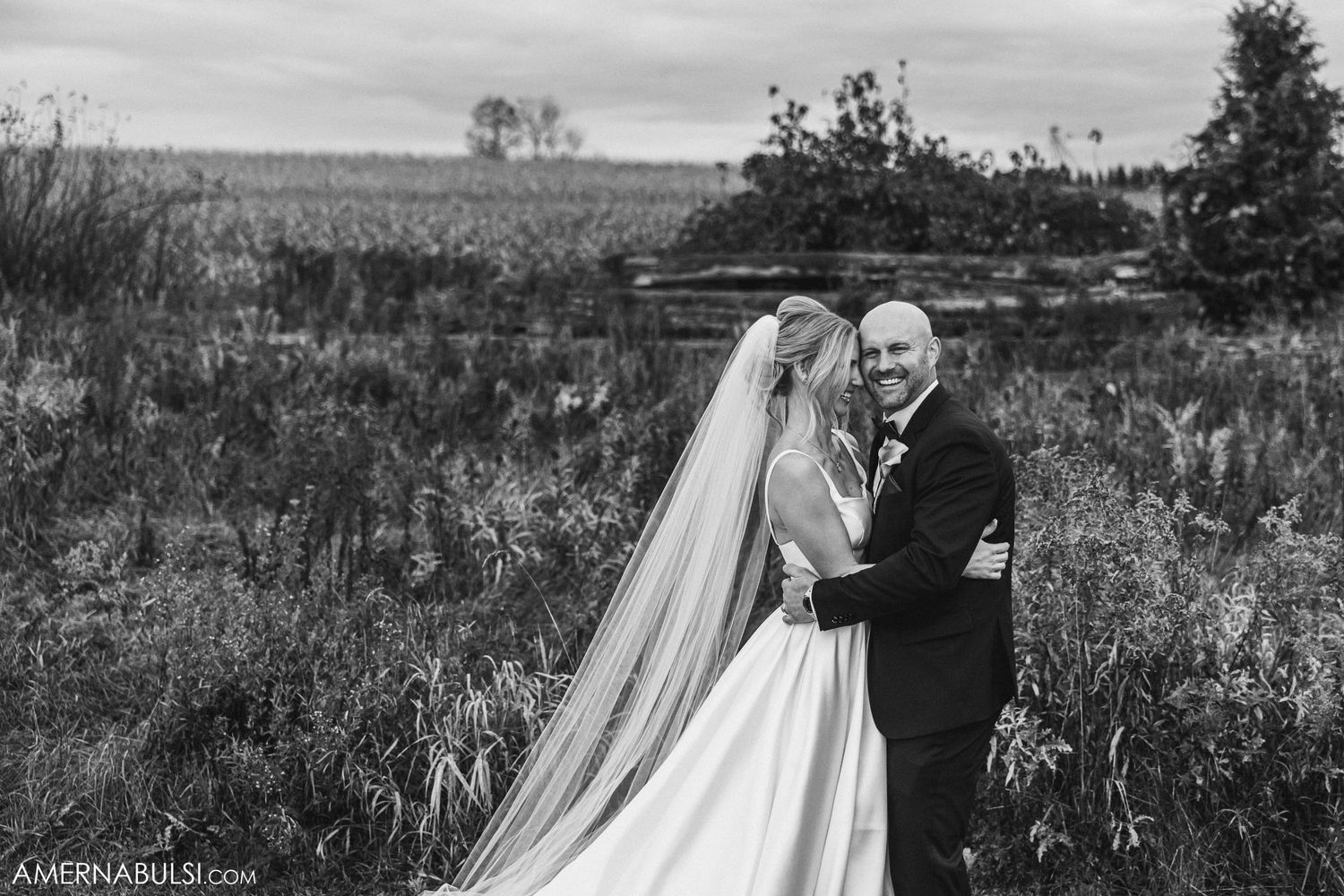 Black and white wedding portrait in a rustic outdoor field setting.