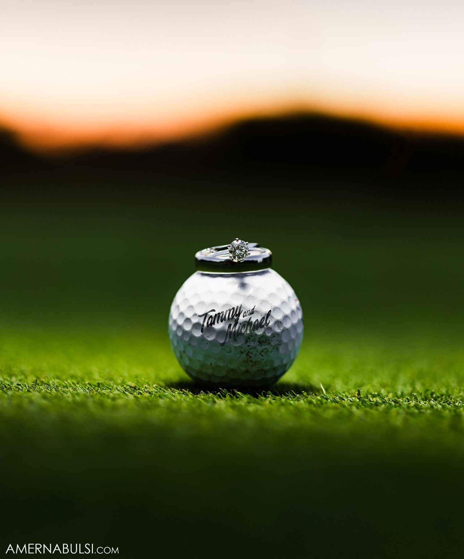 Wedding ring placed on golf ball against sunset backdrop on grass.