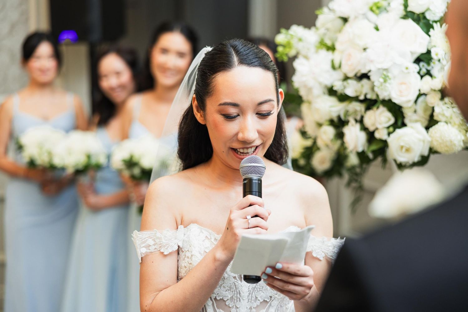 Wedding speech being given in elegant venue with white floral arrangements.