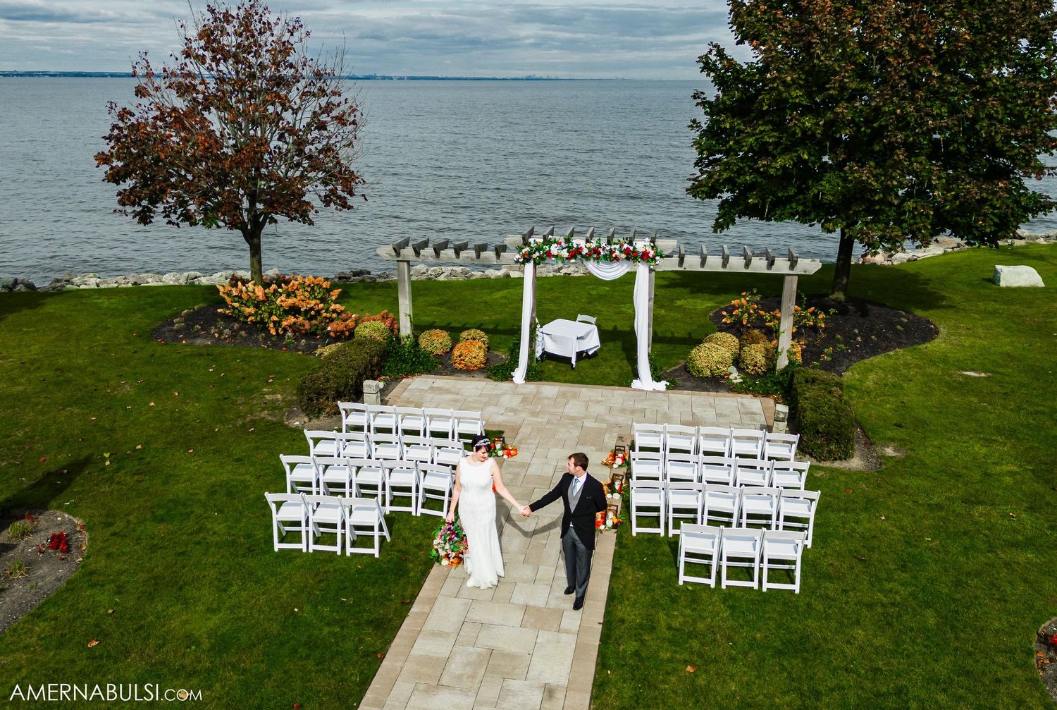 Waterfront wedding ceremony setup with white chairs and pergola overlooking the ocean on a beautiful autumn day.