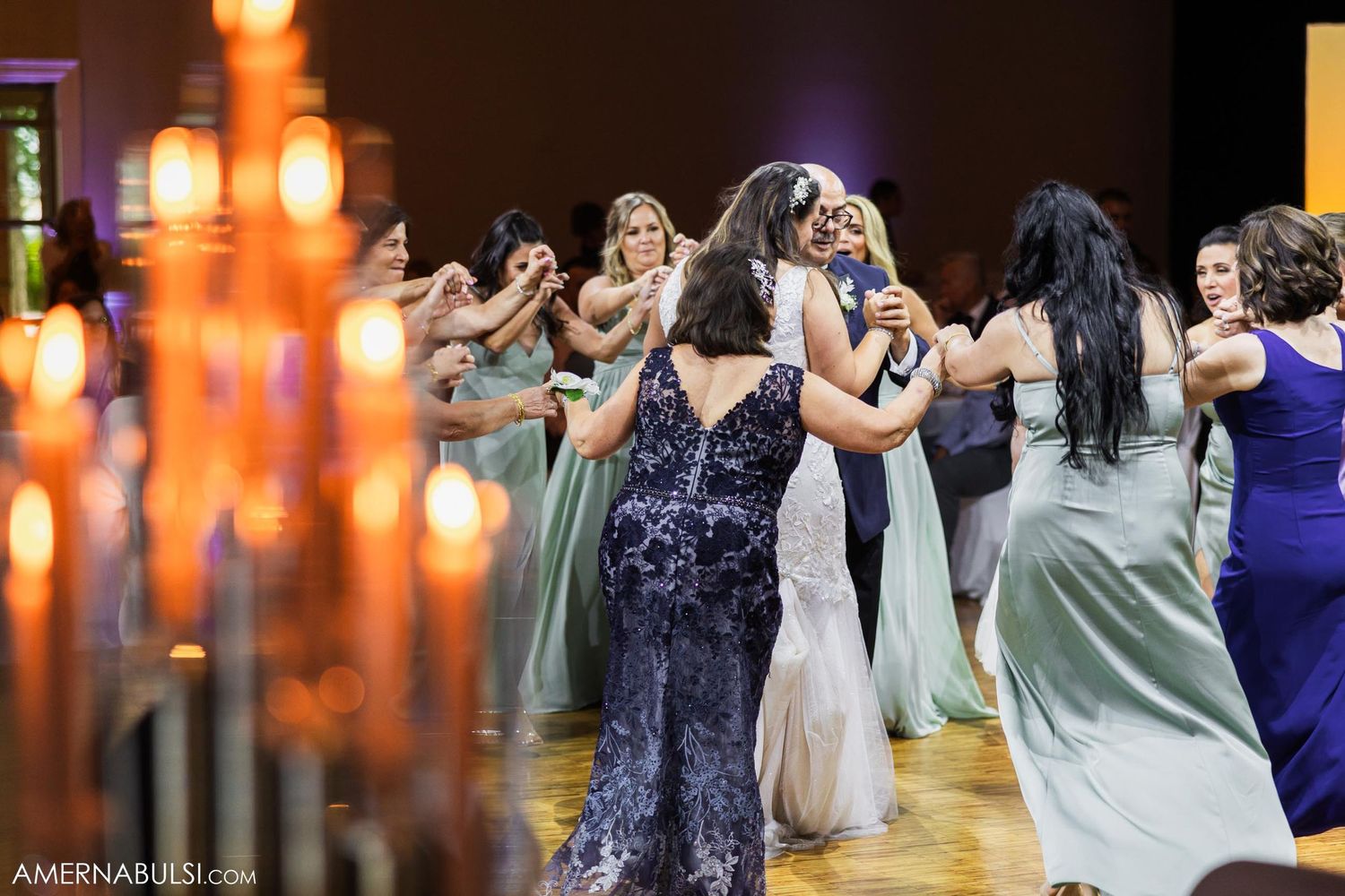Wedding guests in colorful dresses dancing together with candles in the foreground.