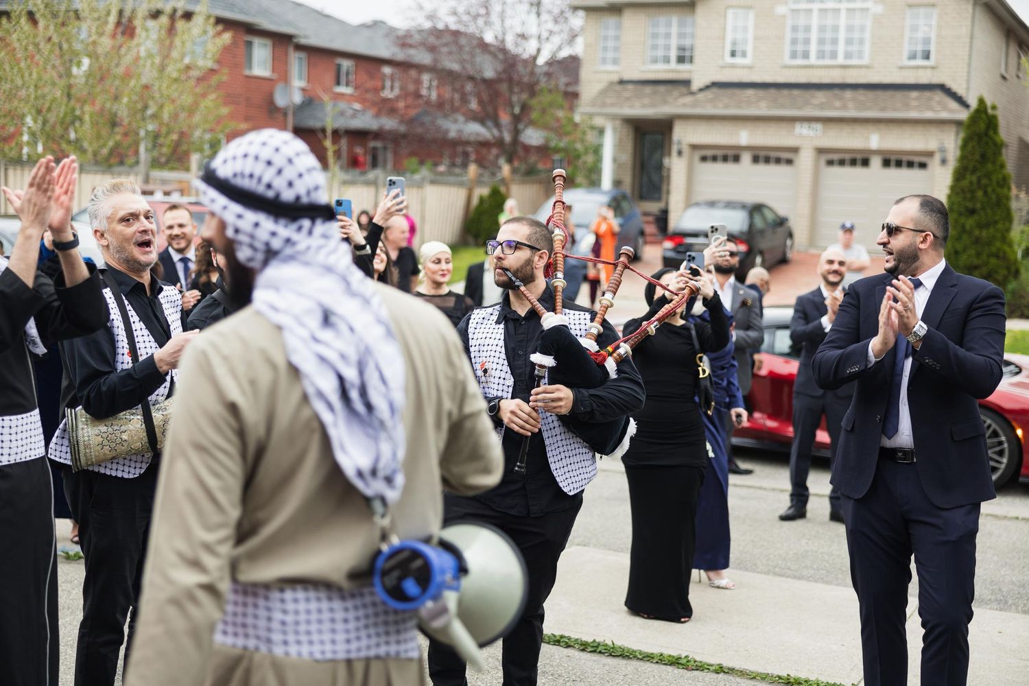 A festive wedding celebration takes place outside with guests cheering in a suburban neighborhood.