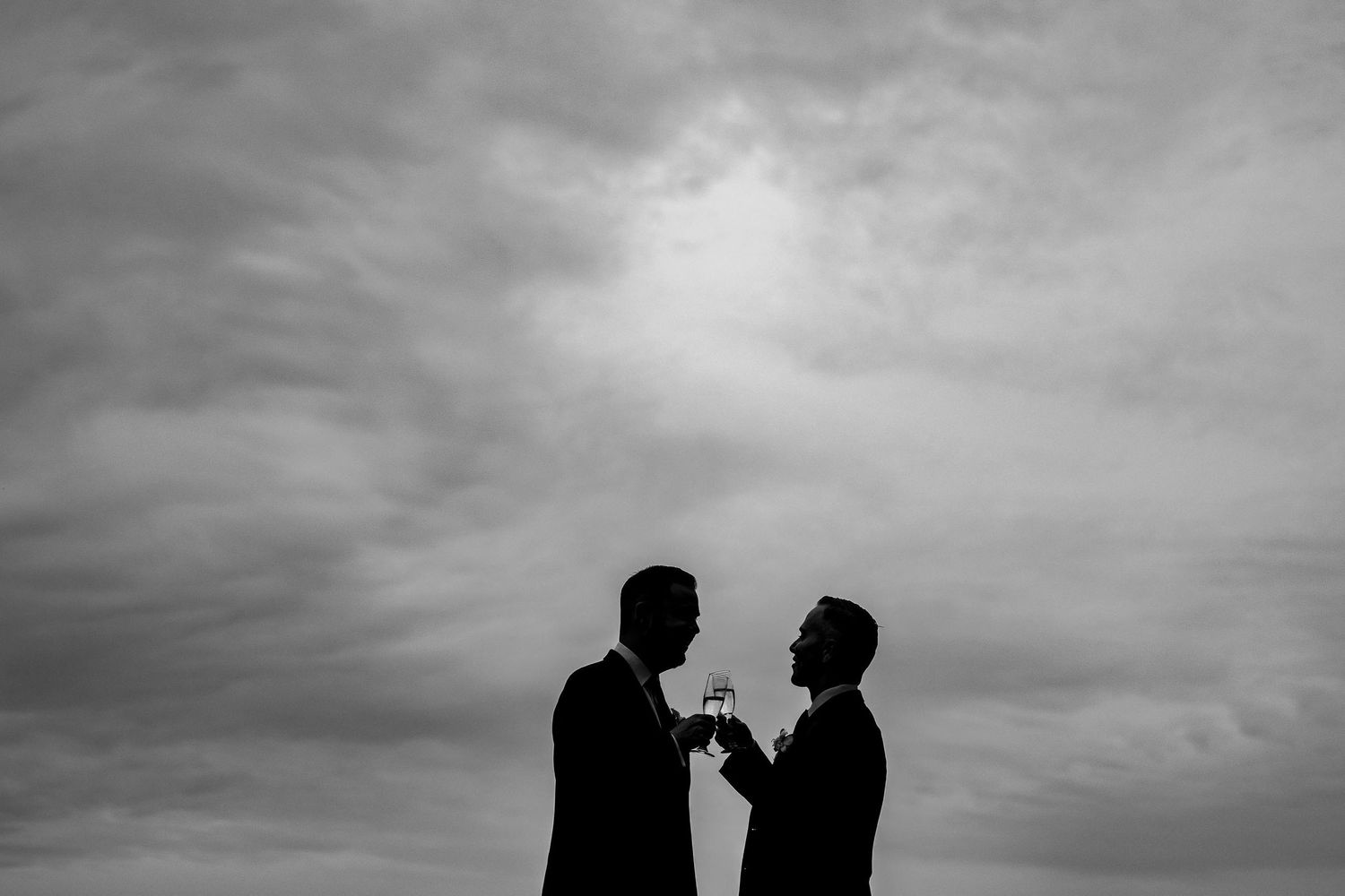 Silhouetted figures against dramatic cloudy sky in black and white.