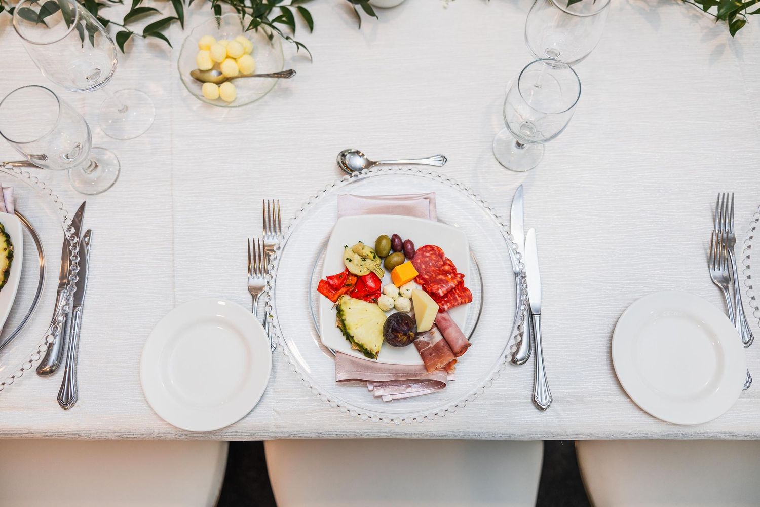 Elegant place setting with plated dinner and formal silverware arrangement on white tablecloth.