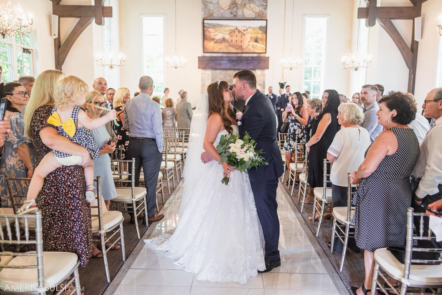 Newlyweds share moment in aisle as guests look on in elegant wedding venue.