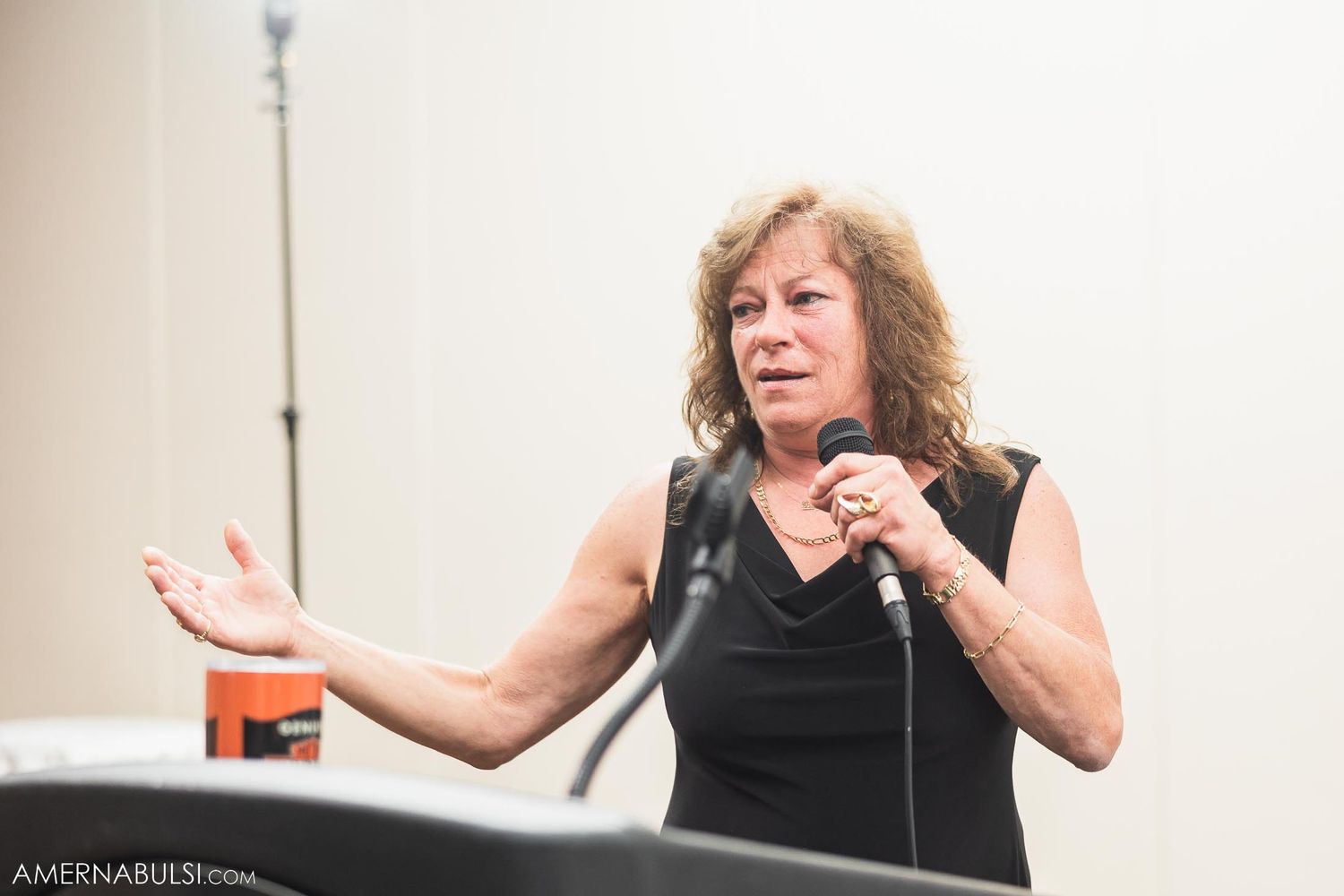 Speaker in black dress gestures while giving speech at wedding reception.