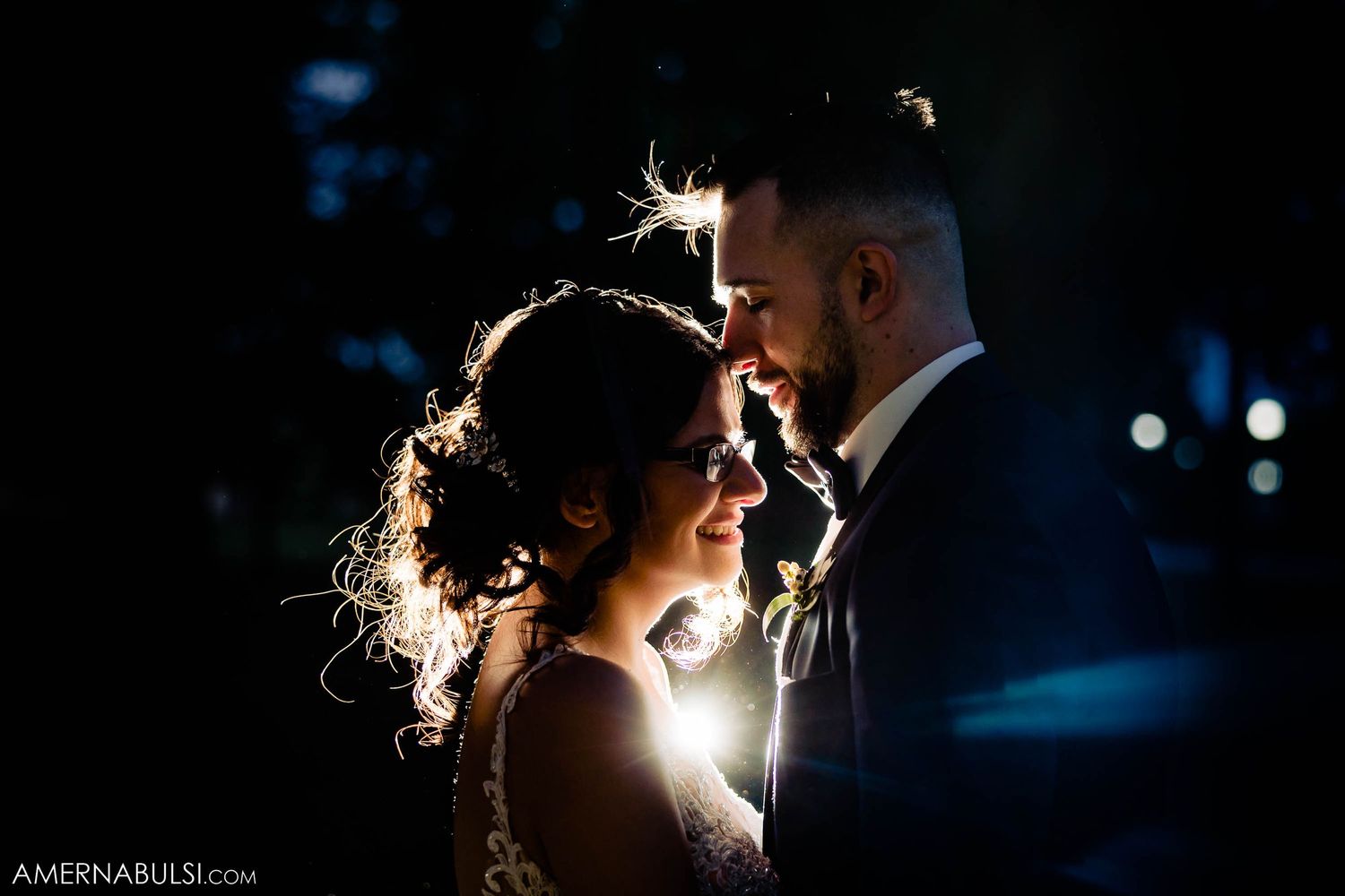 Intimate backlit portrait of couple in formal attire against dark background.