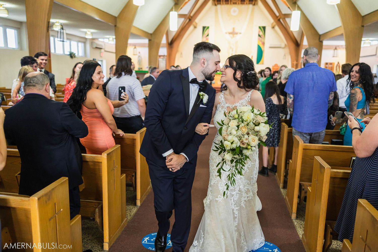Wedding couple shares intimate moment in church aisle surrounded by smiling guests.