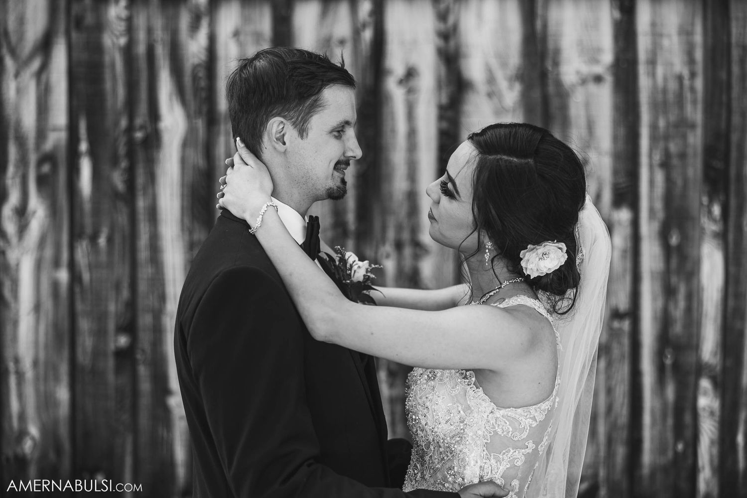 Black and white portrait of newlyweds in an intimate embrace against weathered wood paneling.