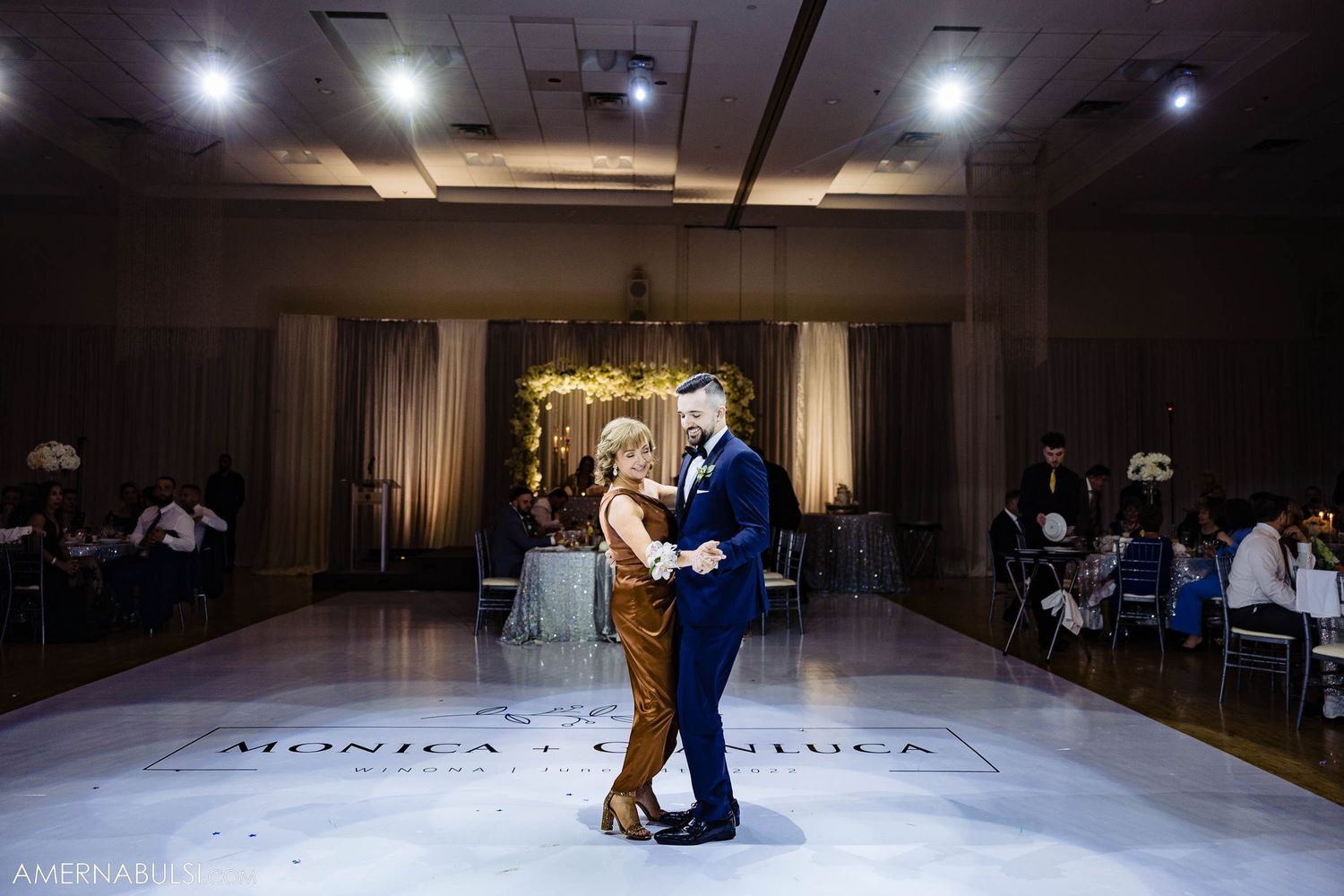 Couple sharing their first dance on an illuminated ballroom floor.