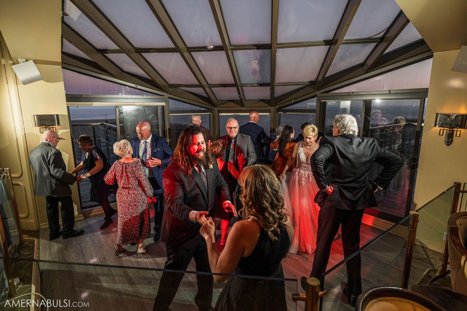 Wedding reception guests dance under warm lighting in an indoor venue.