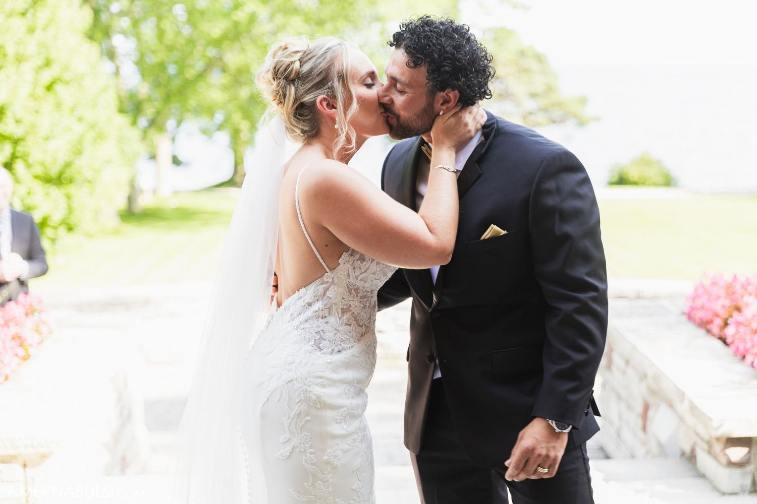 A romantic outdoor wedding moment captured in natural sunlight with greenery in the background.