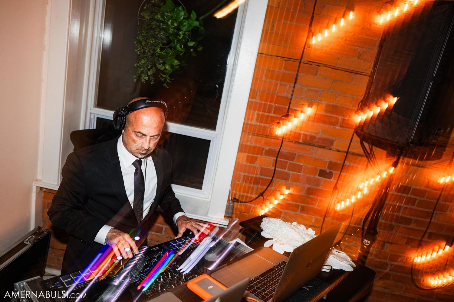 DJ plays music at a wedding reception with string lights in the background.