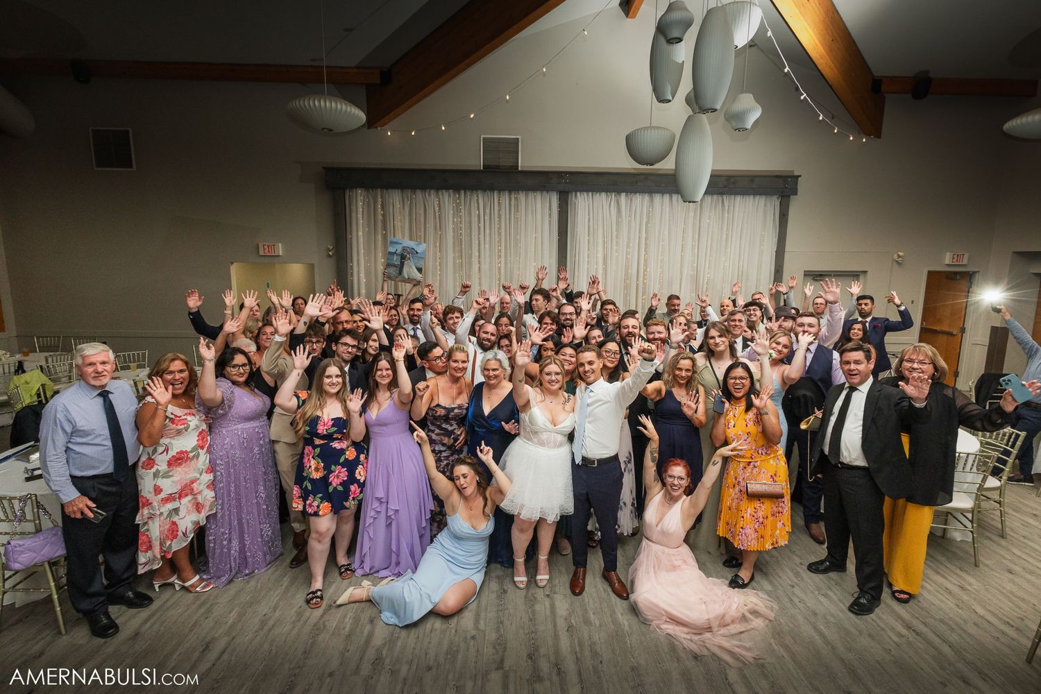 Large group of wedding guests gather on a dance floor for a celebratory photo at a reception venue.