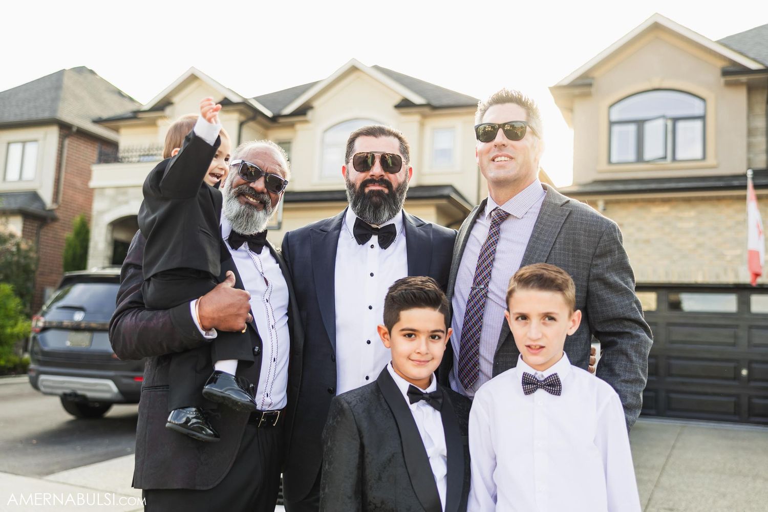 Formal group photo in front of suburban homes wearing suits and sunglasses.