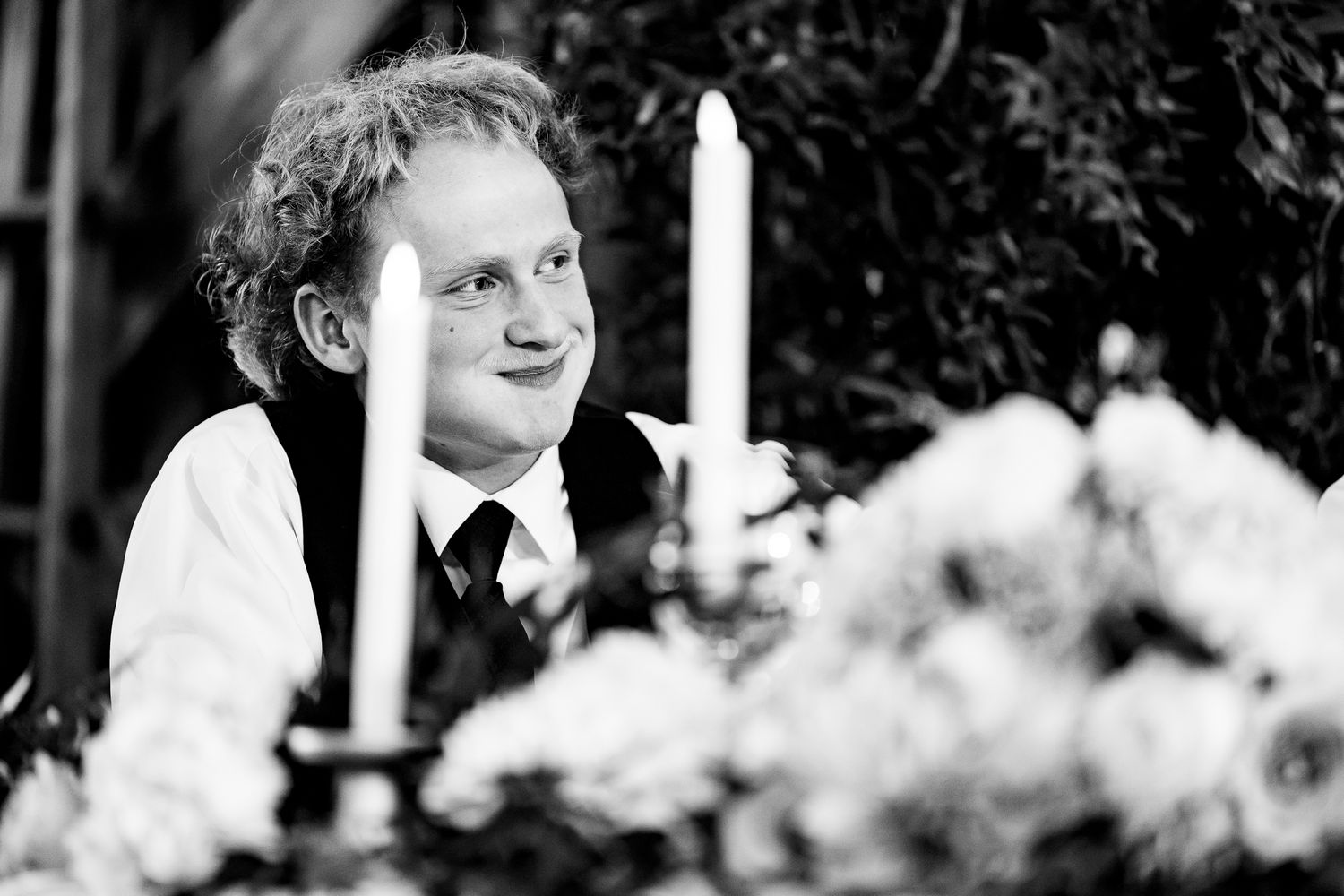 Two people share an intimate moment among white flowers during an outdoor celebration.
