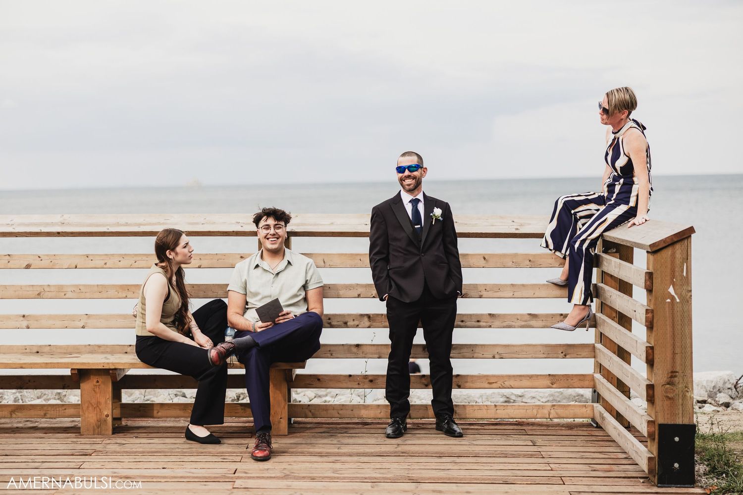 Wedding party members sitting and relaxing on a wooden boardwalk by the beach.