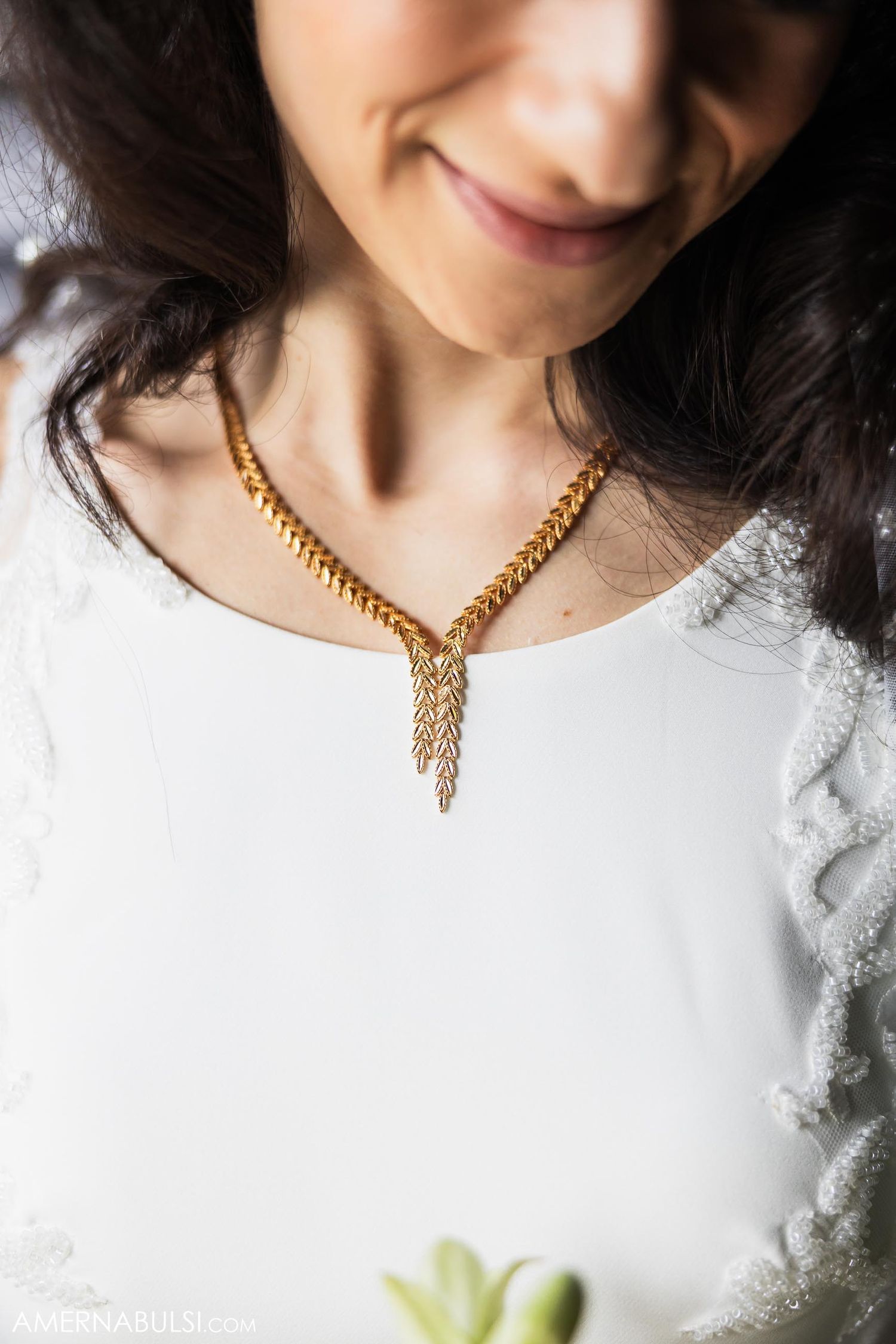 Close-up of a delicate gold chain necklace with tassel detail against white lace fabric.