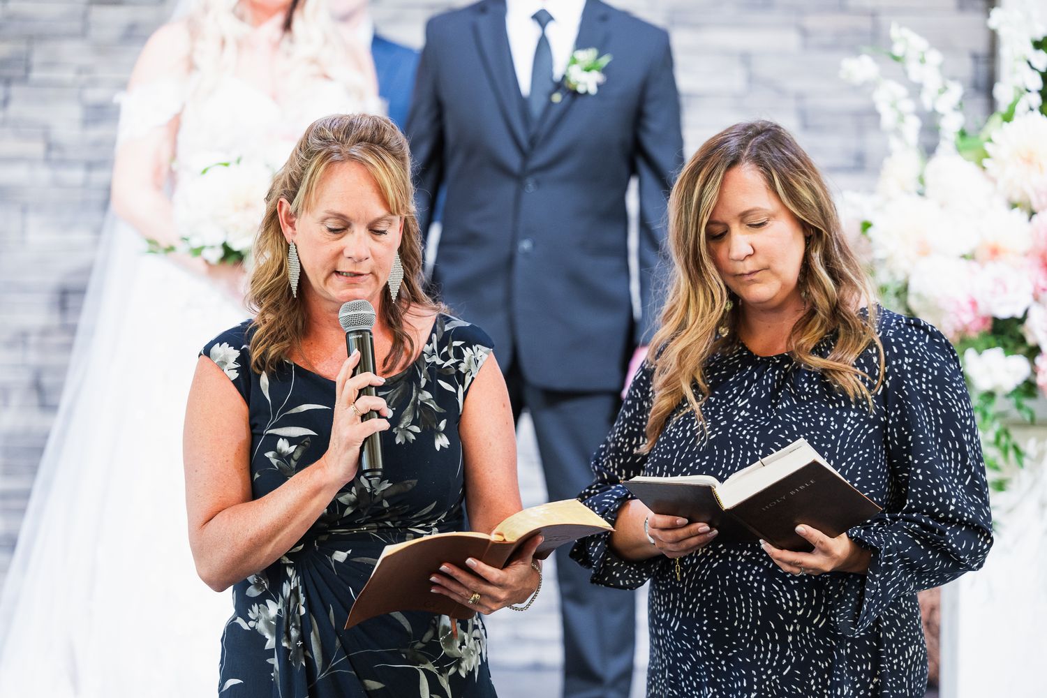Wedding party members gather closely at a modern reception venue wearing formal navy and black attire.