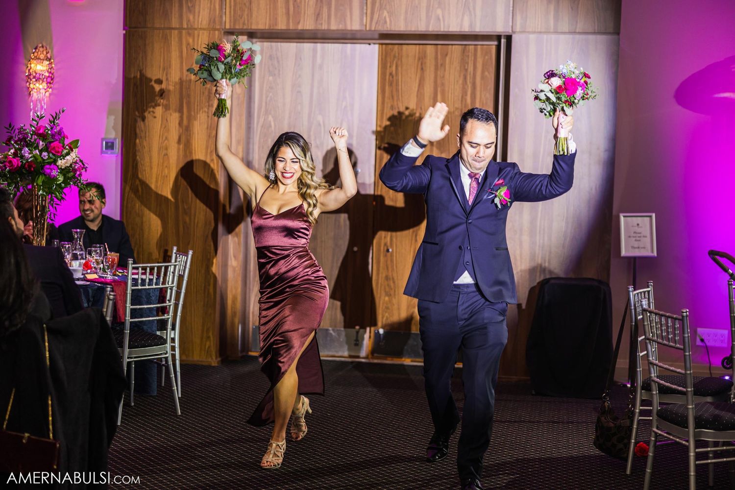 Bridal party members making energetic entrance at reception with floral bouquets.