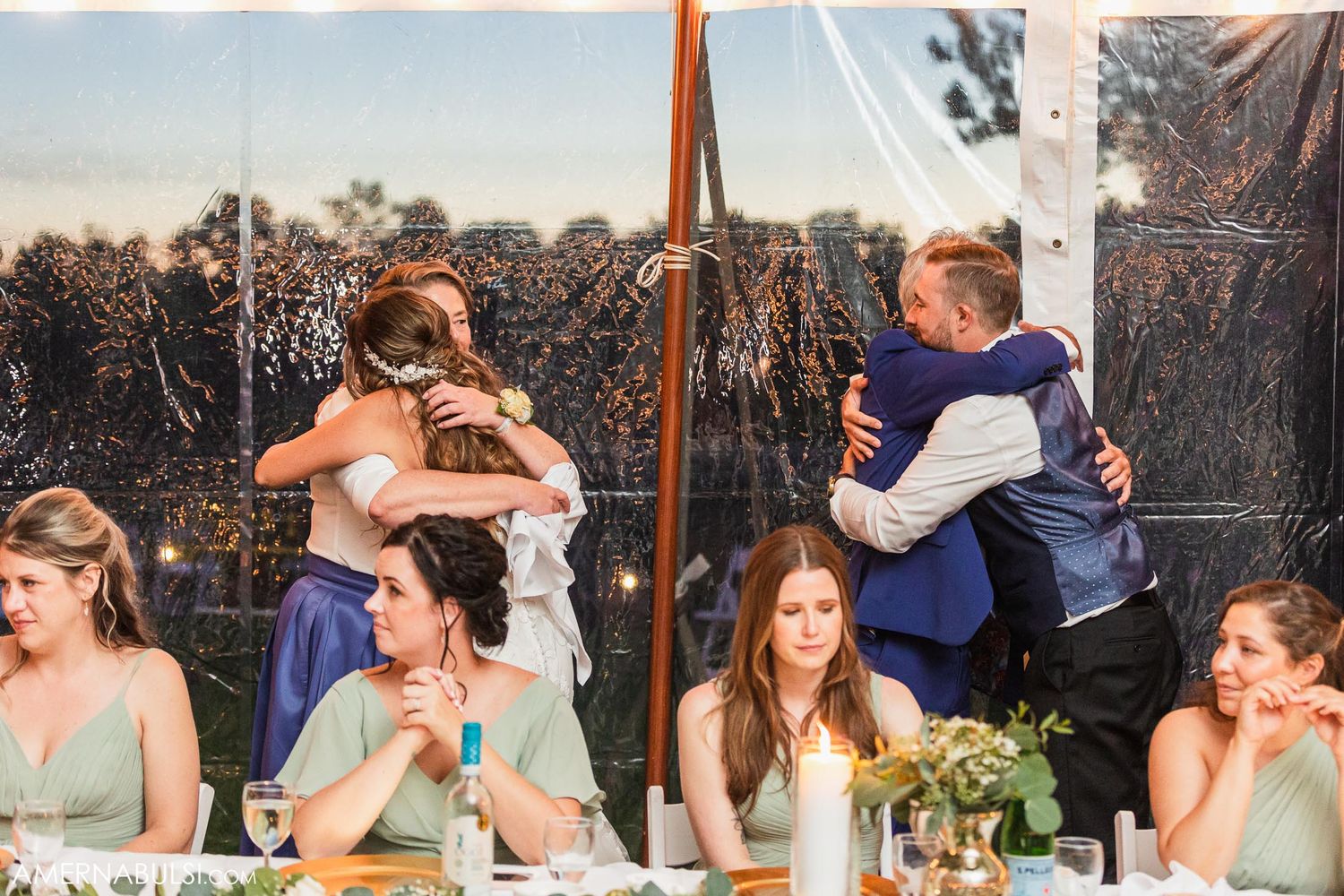 Wedding party members share embraces while others watch from the head table.