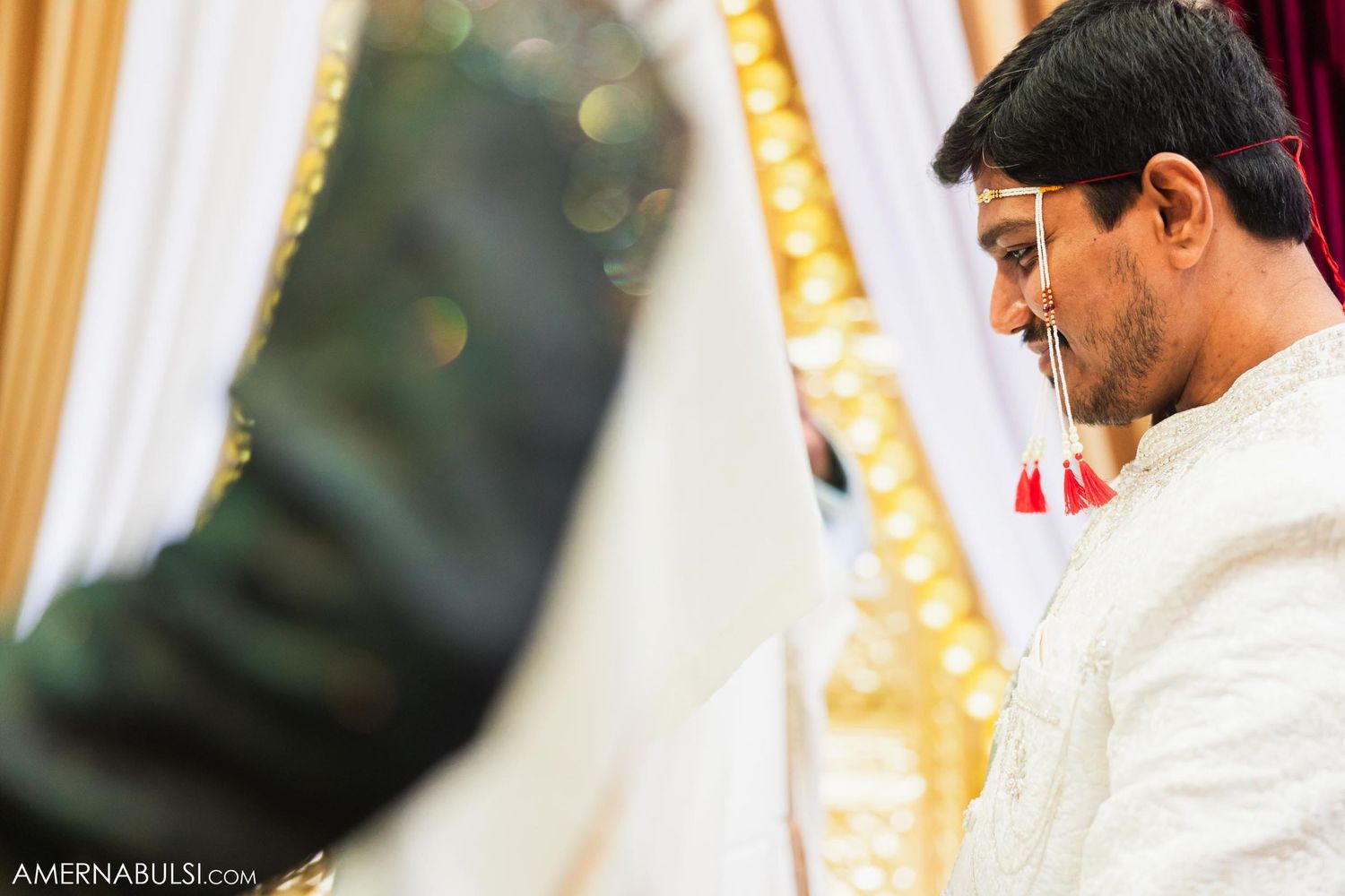 Close-up profile shot of someone wearing traditional white Indian wedding attire against soft bokeh lights.