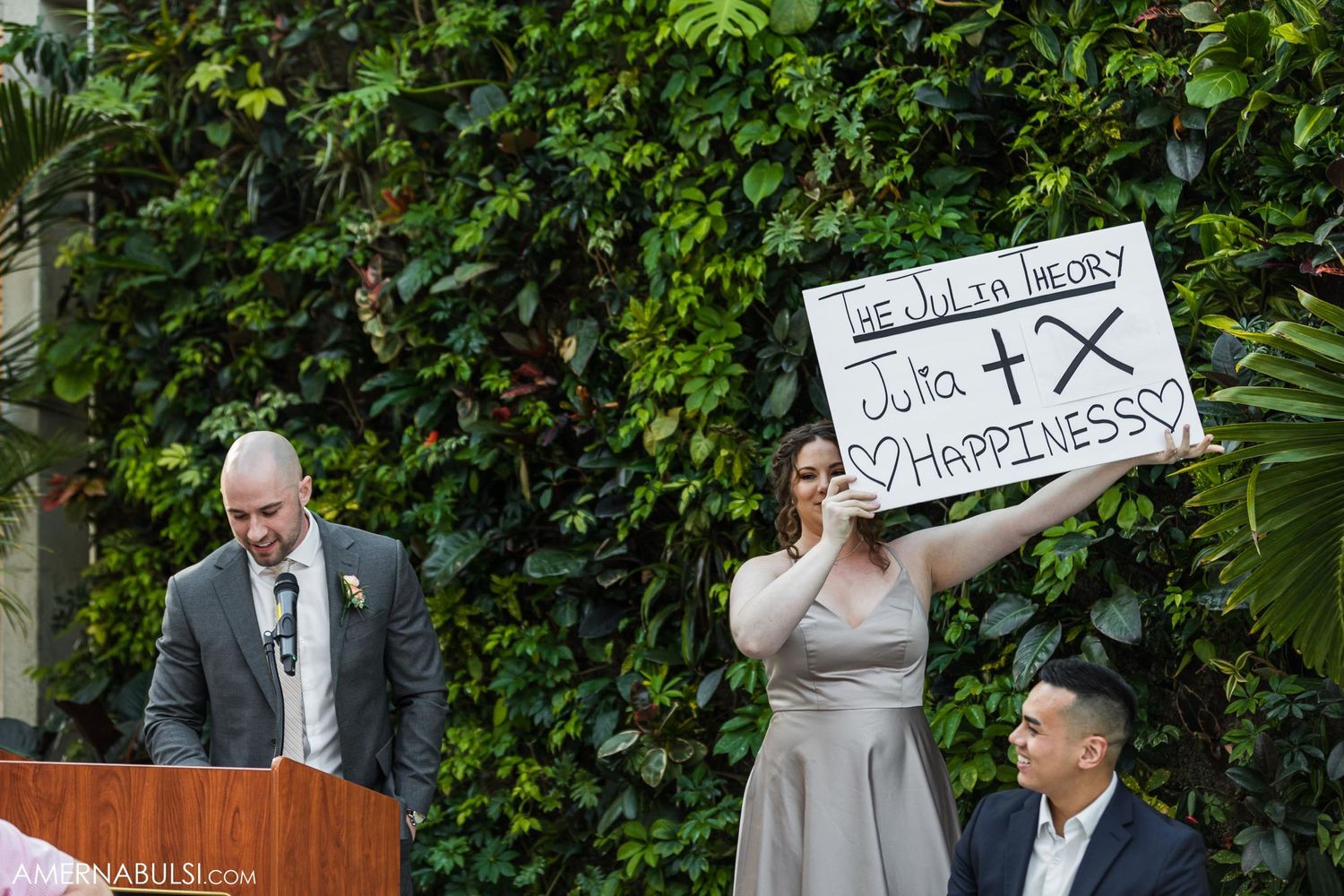 A wedding guest holds up a humorous sign during an outdoor ceremony speech.