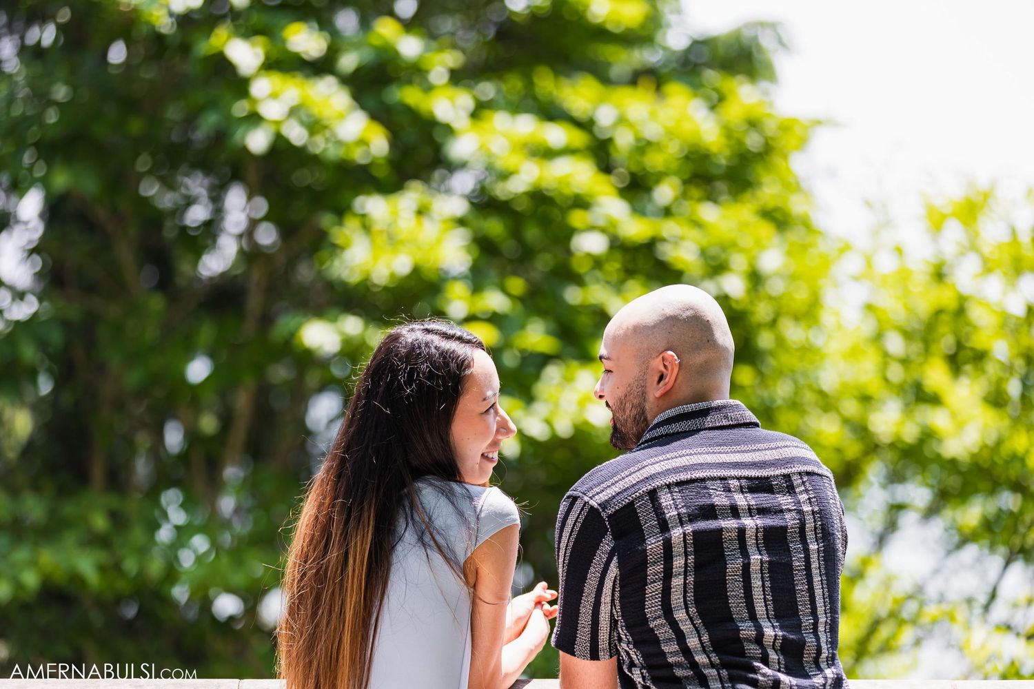 Intimate couple sharing a tender moment while standing on a balcony against green foliage.
