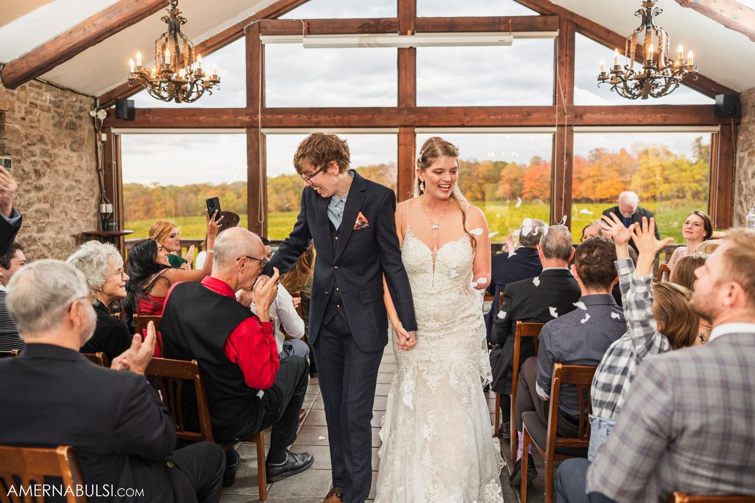 Wedding ceremony recessional in rustic venue with exposed wooden beams and large windows.