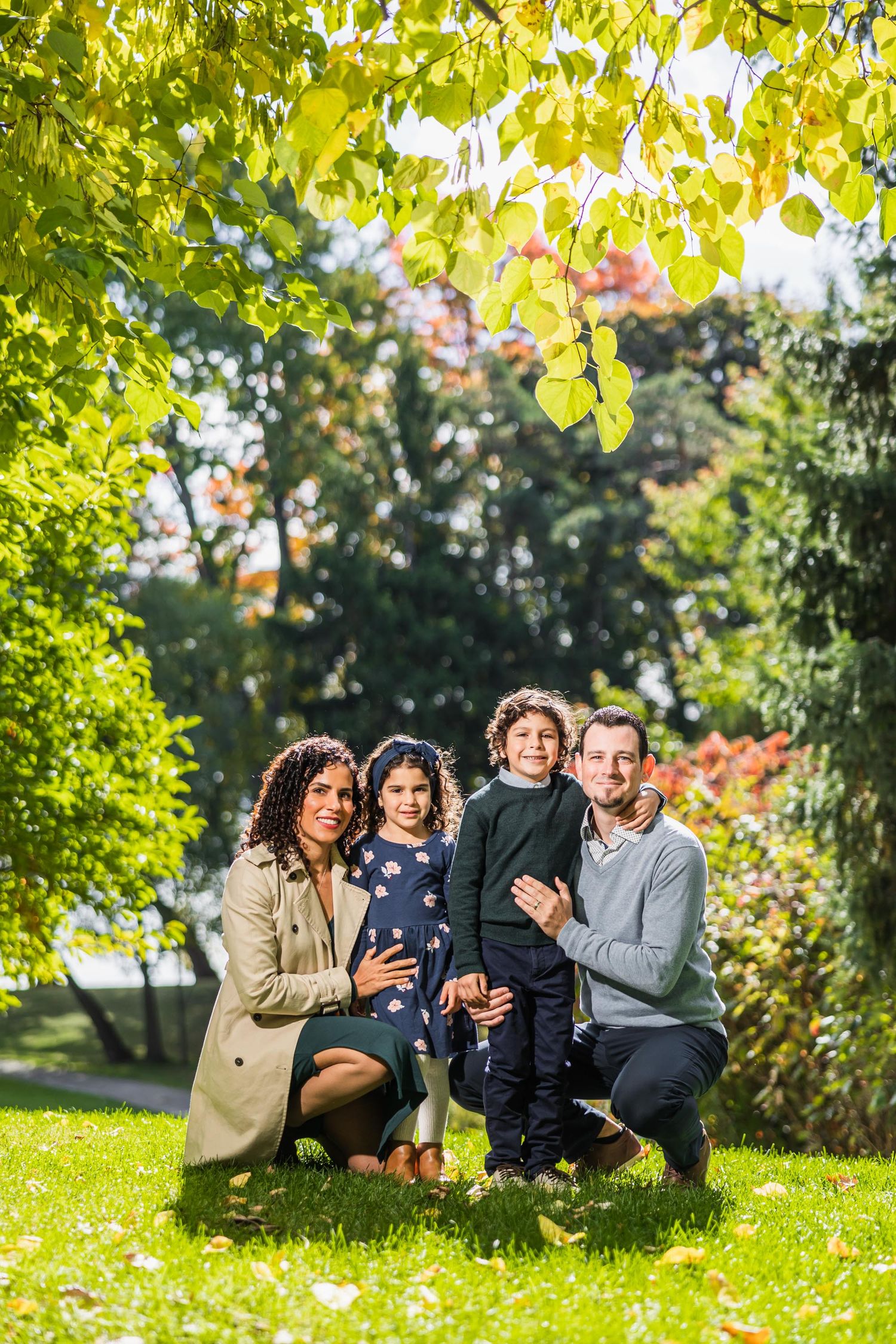 A family portrait under sunlit autumn trees in a lush garden setting.
