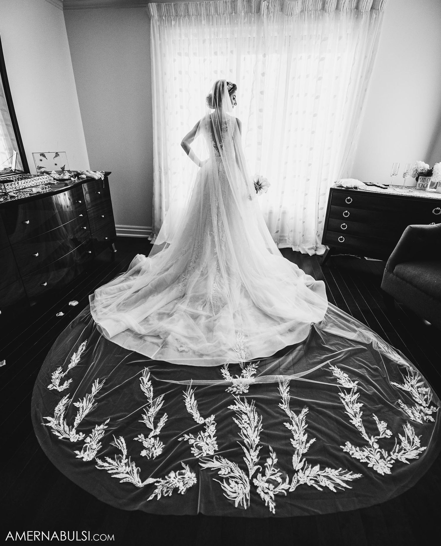 Dramatic black and white silhouette of bride with ornate train detail against window.