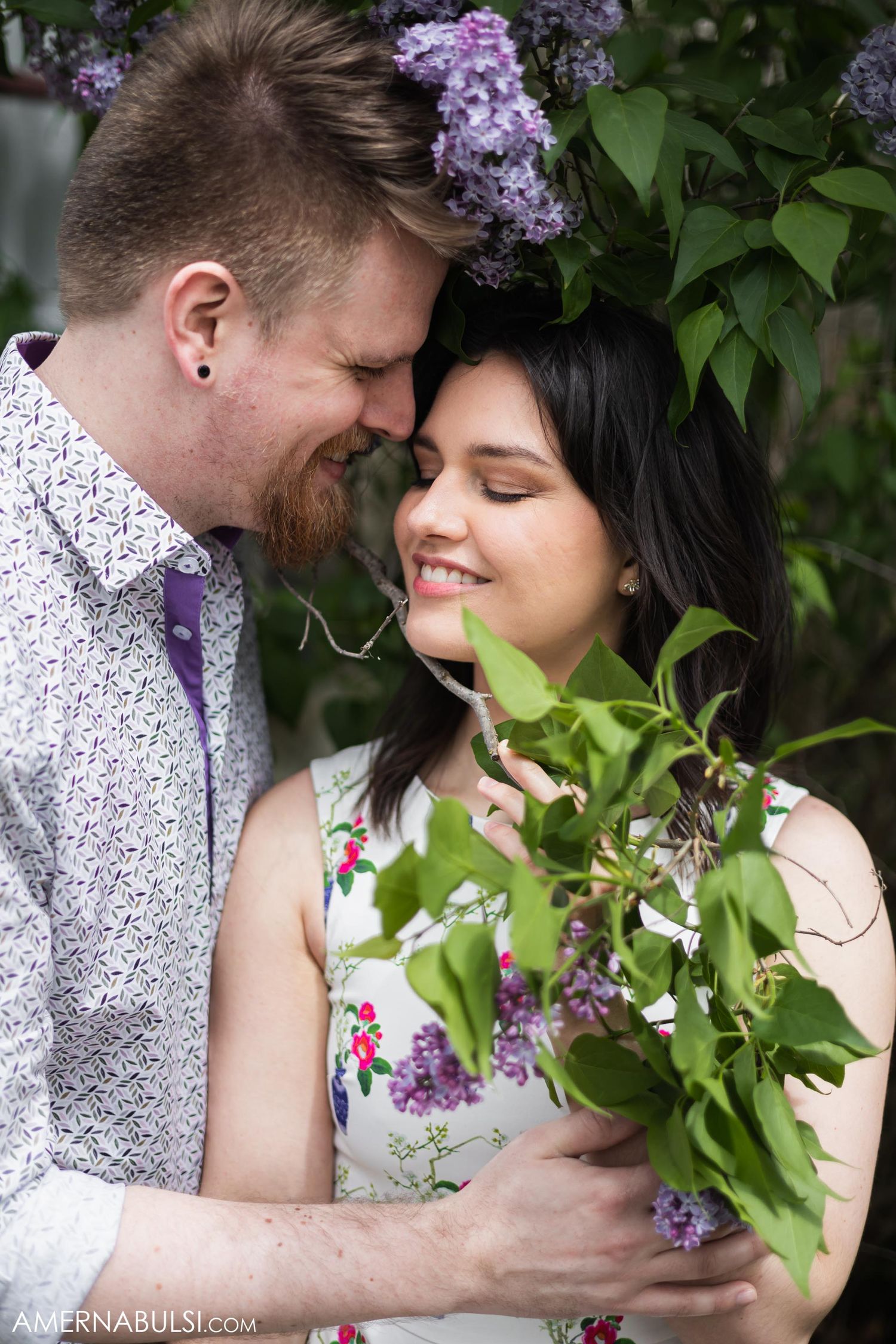 Romantic spring portrait with couple among blooming lilac bushes in garden setting.