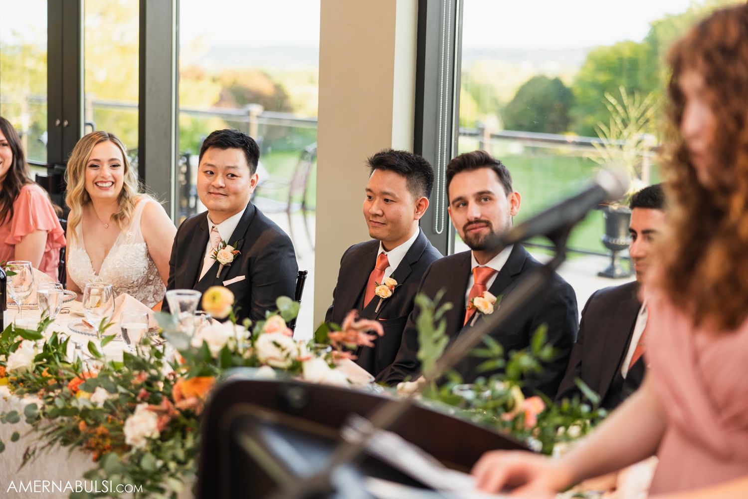 Wedding reception guests seated at decorated table with floral centerpieces.