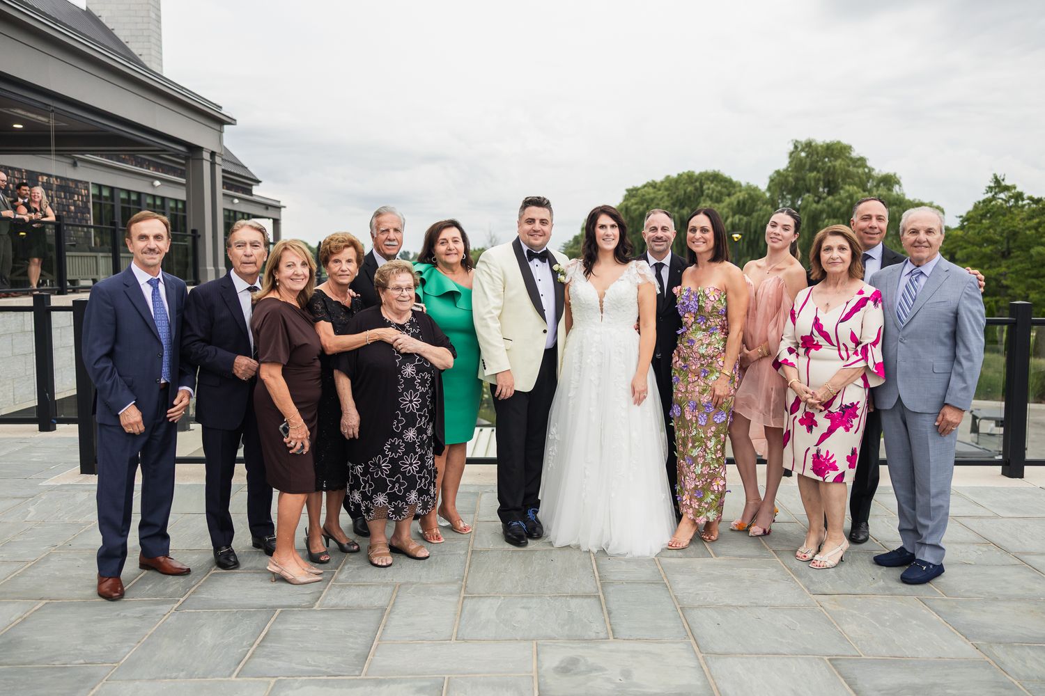 Large family group portrait with bride and groom on an outdoor terrace at a wedding reception.