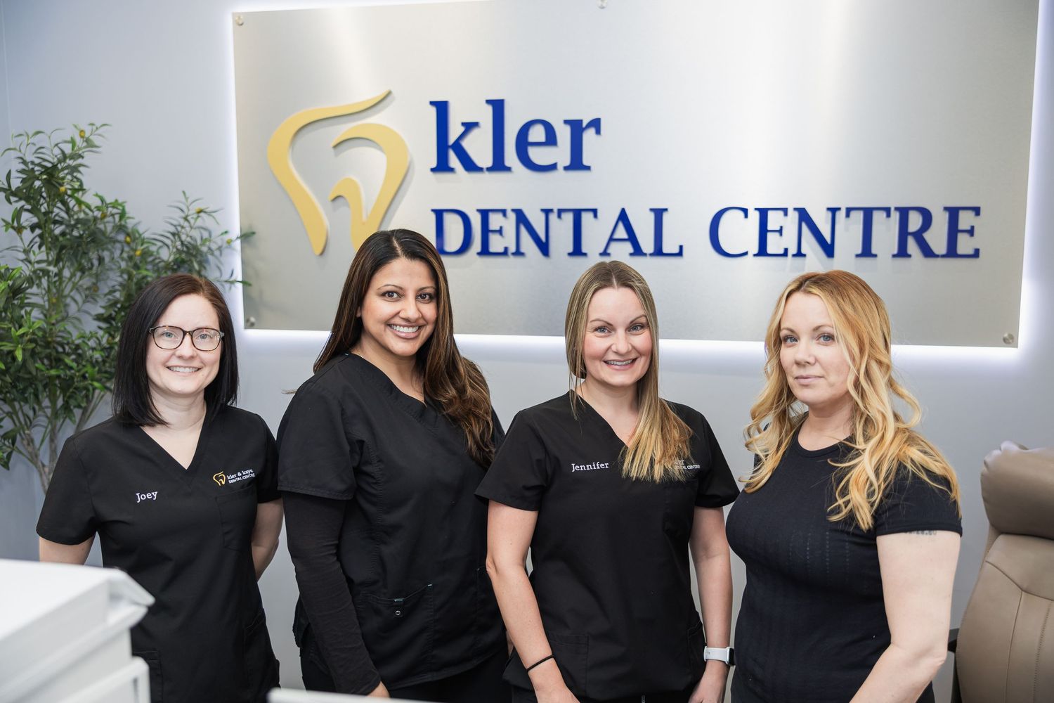 Four smiling dental staff members in black scrubs standing together at Kler Dental Centre reception area.