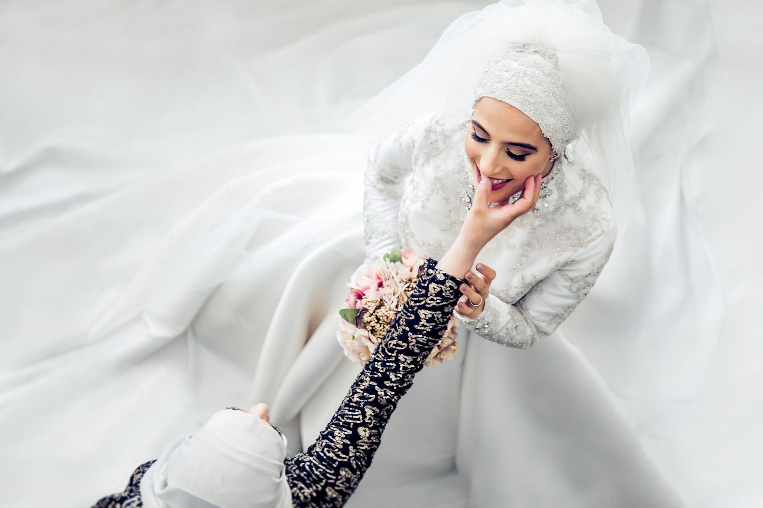 Creative overhead shot of bride lying on white fabric with flowing dress.