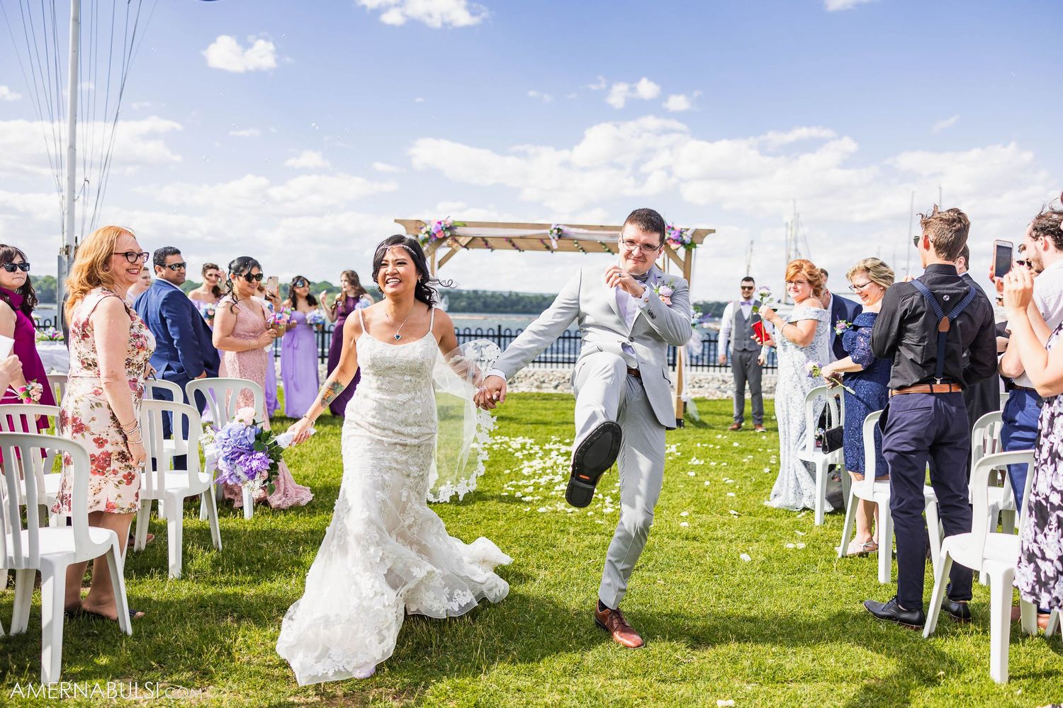 Wedding ceremony celebration with couple walking down outdoor aisle by waterfront.