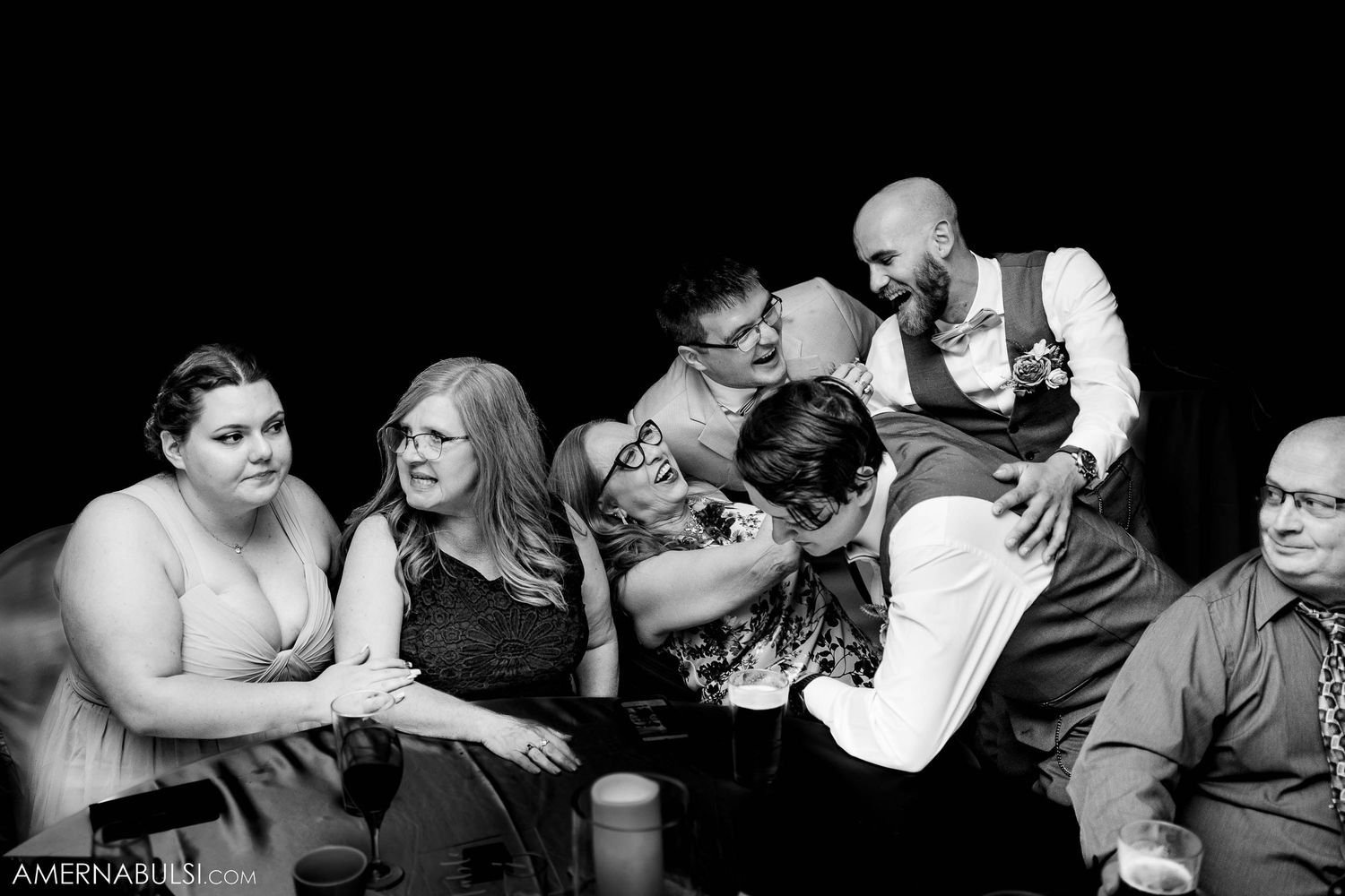 Black and white candid photo of wedding guests sharing laughs at reception.